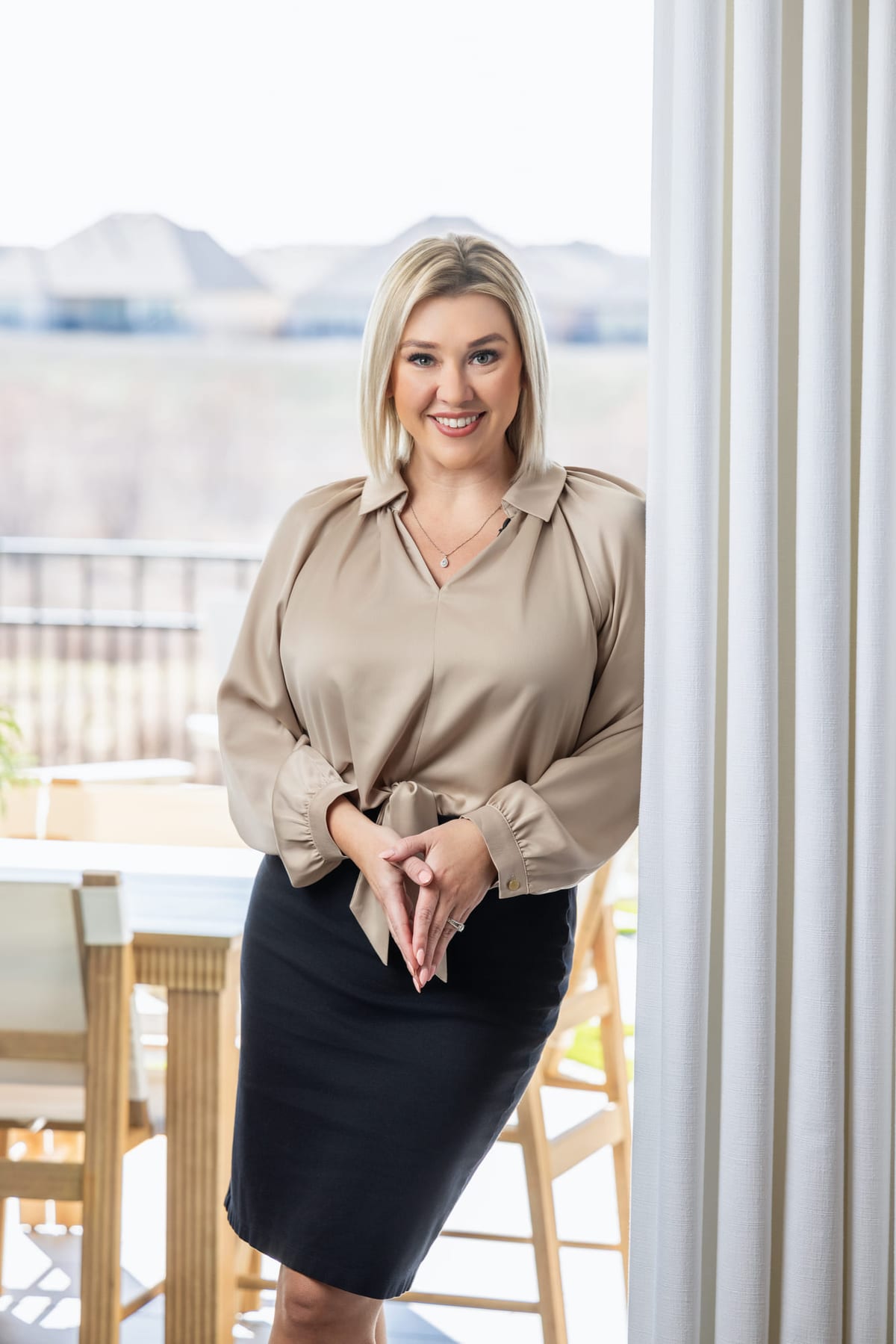 A business portrait beside a white column, hands folded.
