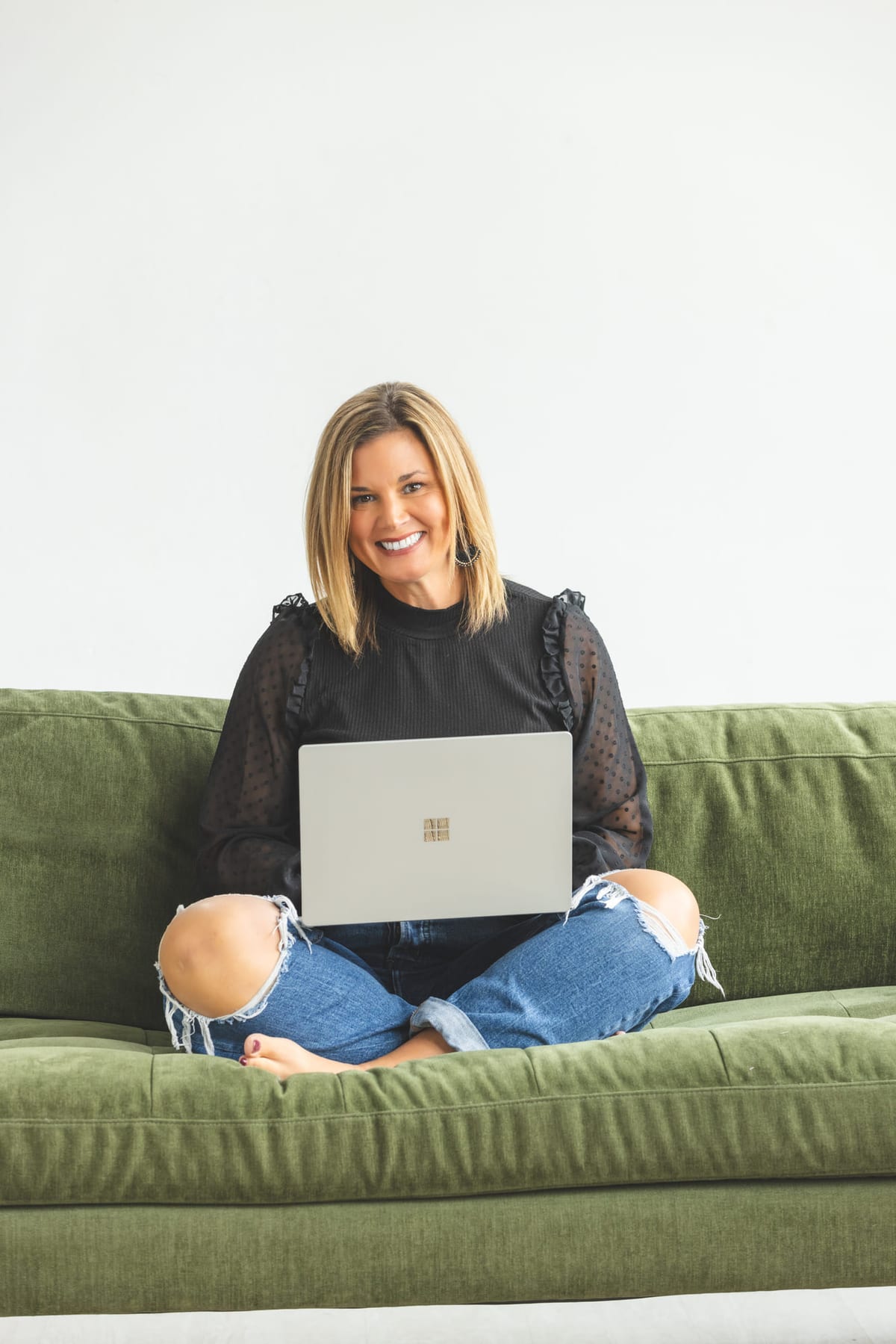 A brand portrait cross-legged on a green sofa with a laptop.
