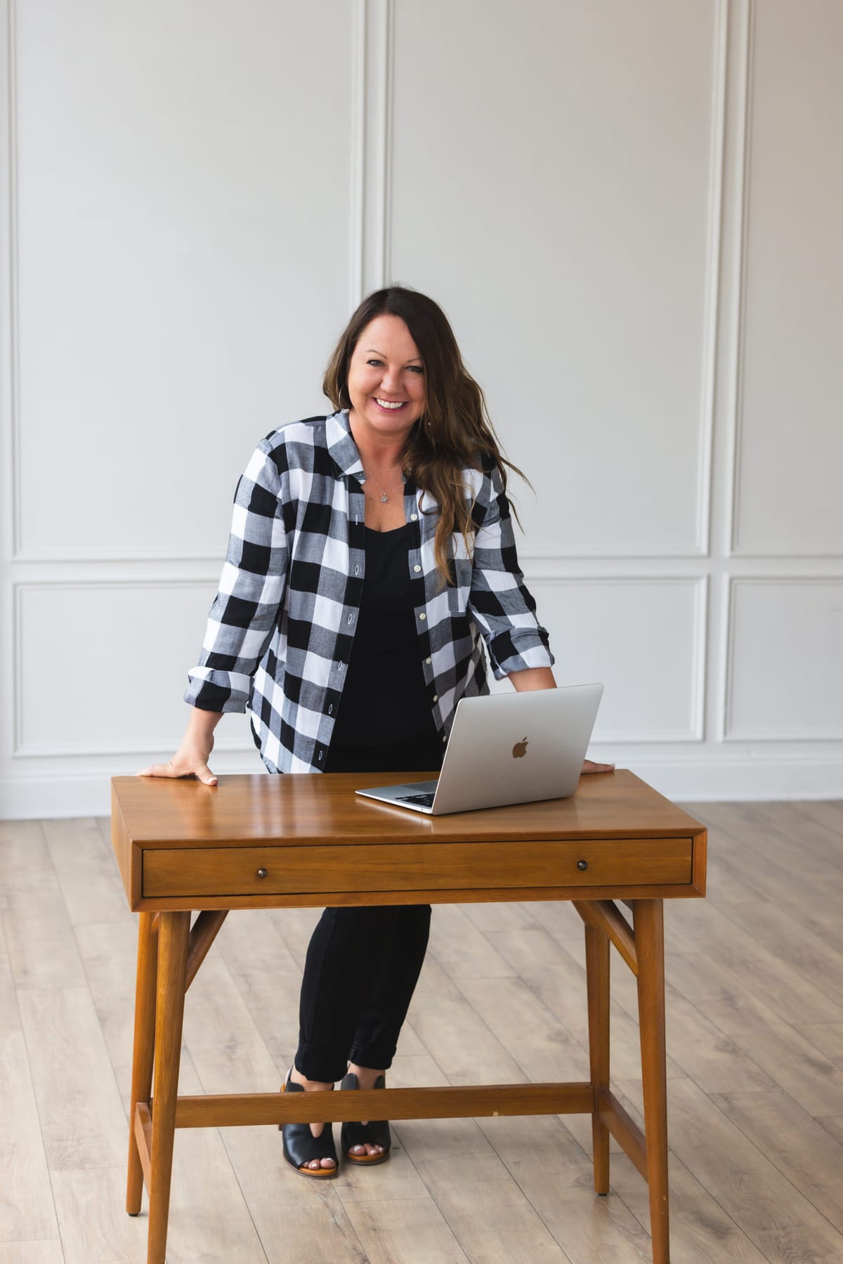 A brand portrait standing at a walnut desk with an open laptop.