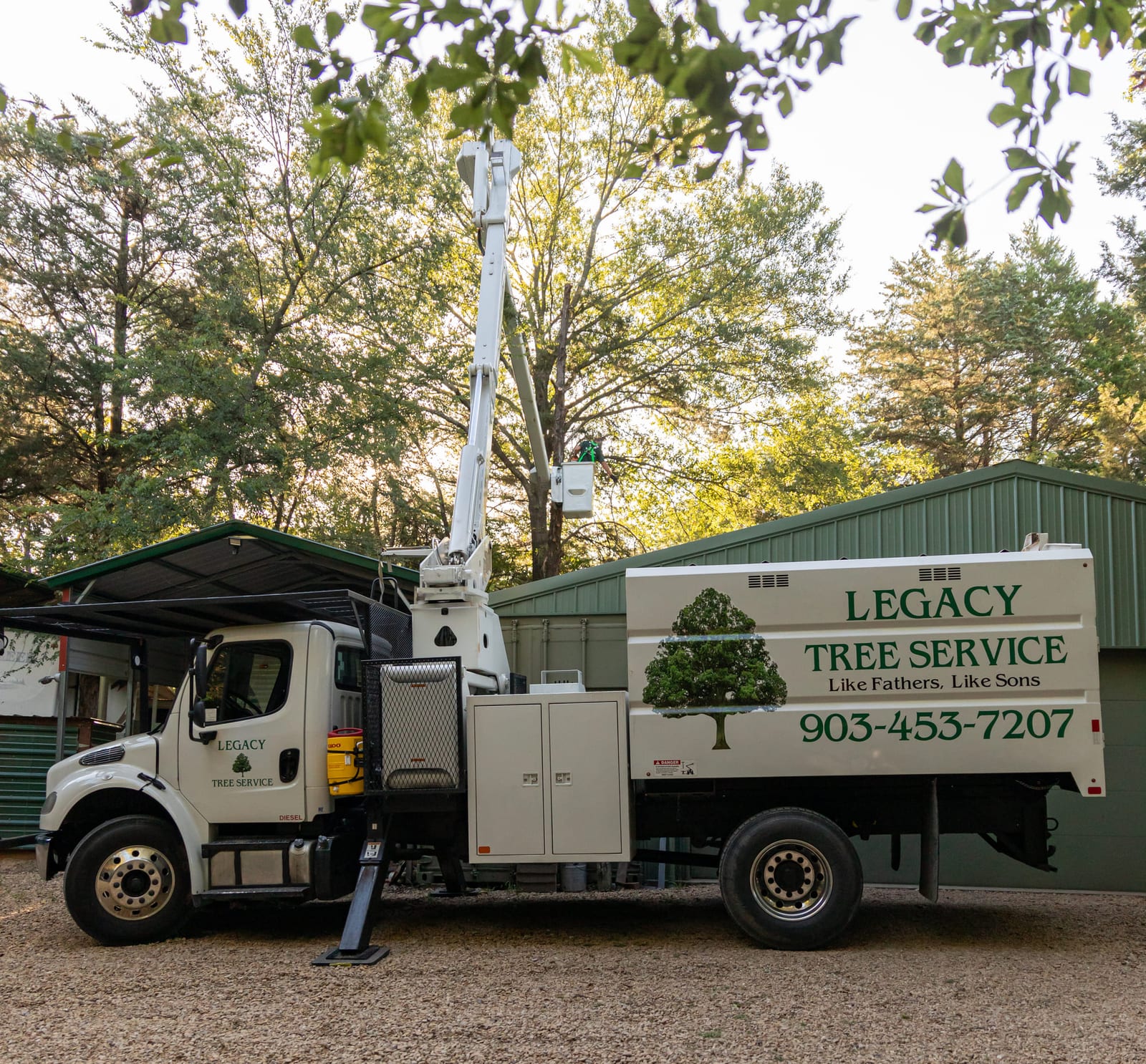 A tree-service bucket truck parked under trees, the company name lettered on the door.