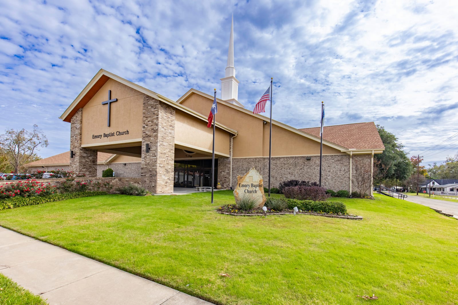 A church exterior with its steeple and cross against a broken sky.