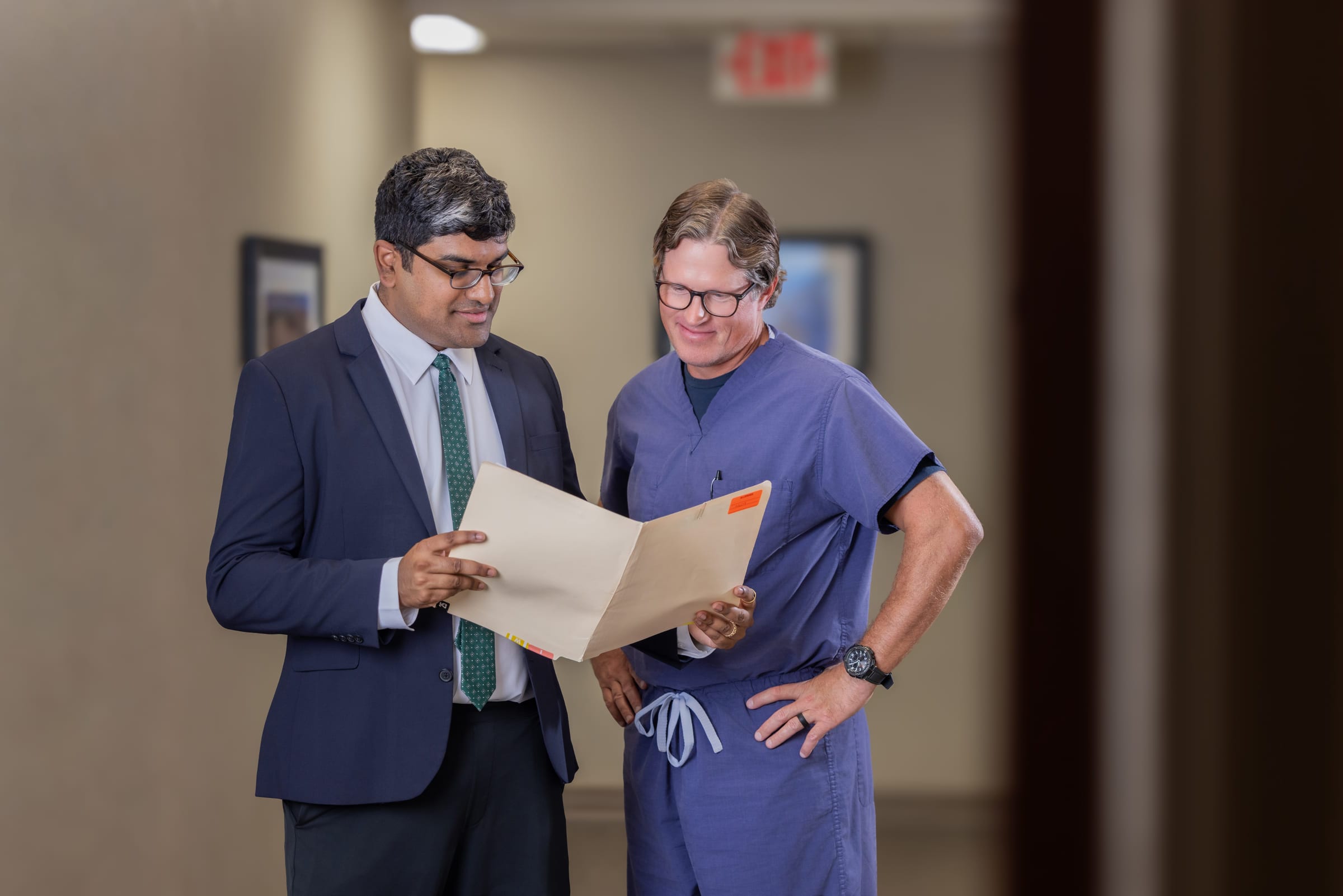 Two clinicians conferring over a file in a clinic corridor.