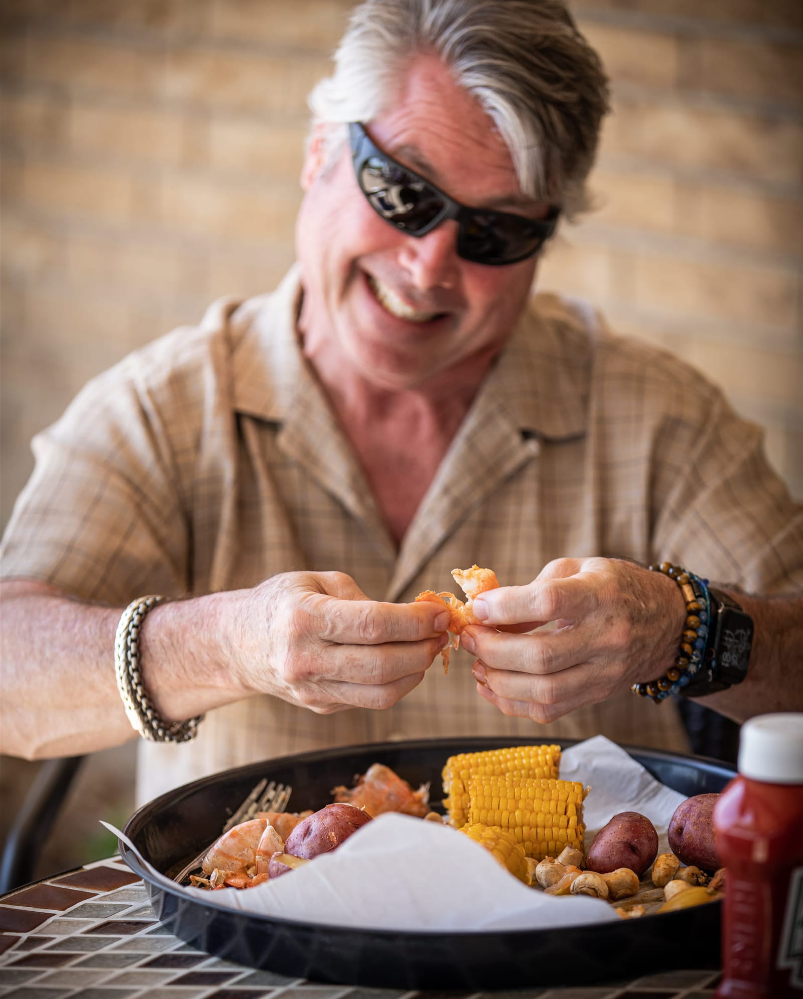 A diner shelling crawfish over a tray of corn and sausage.