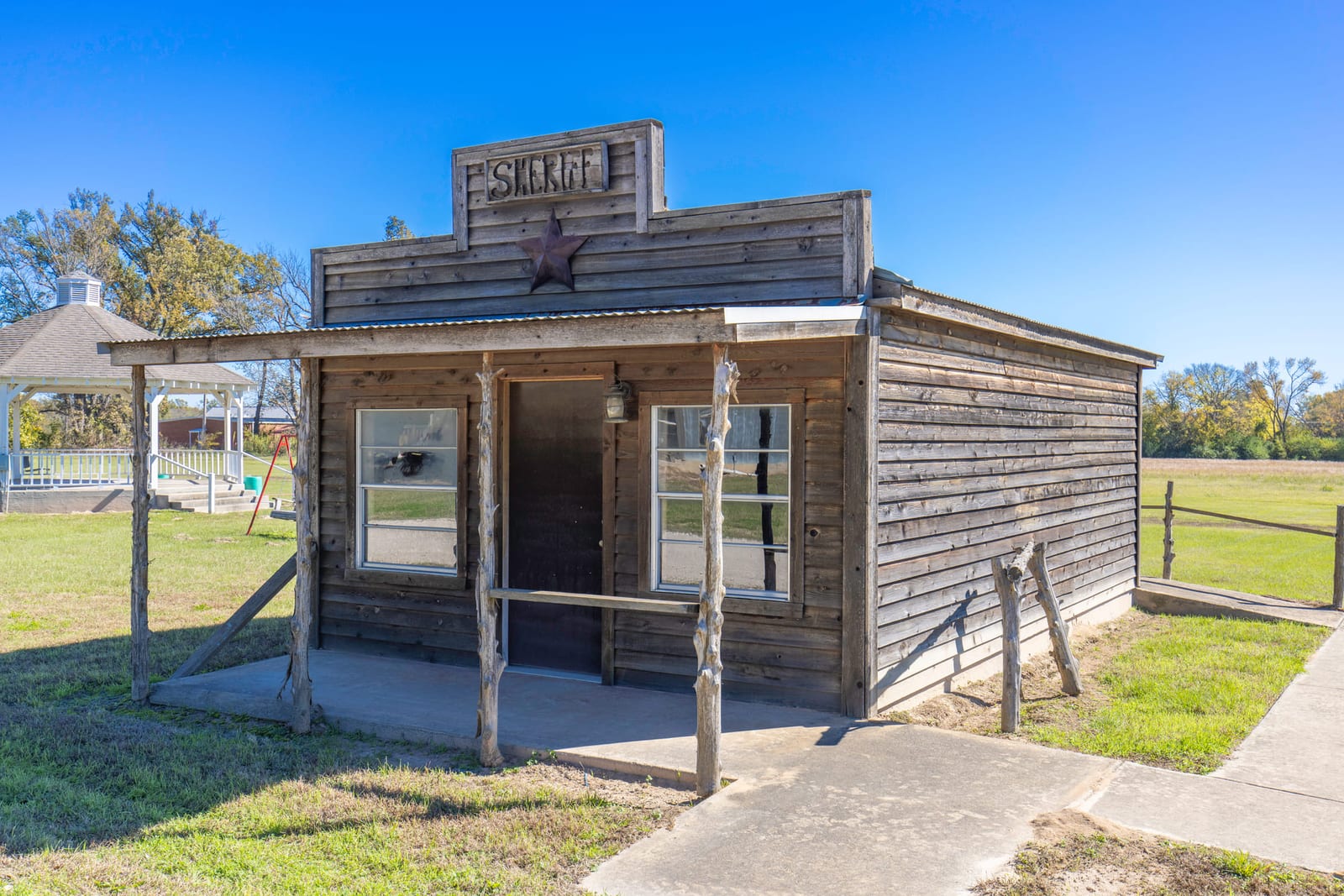 A restored timber store building with a covered boardwalk, standing alone on mown grass.