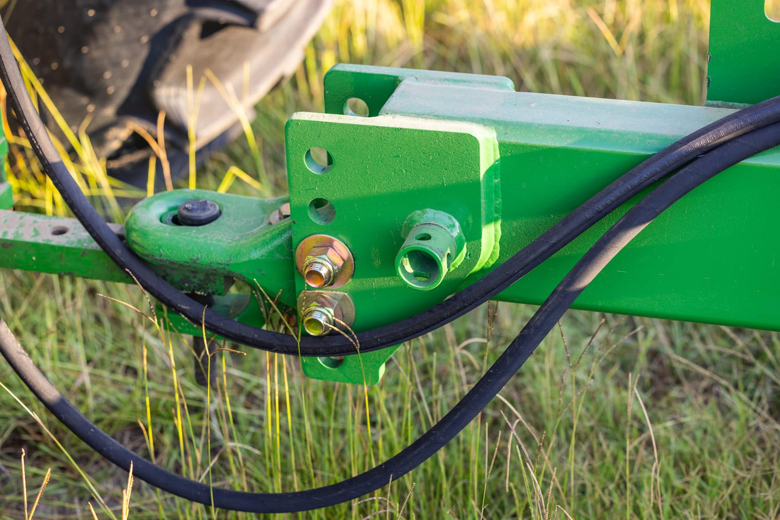 A close frame of hydraulic fittings on a green farm implement, grass in the foreground.