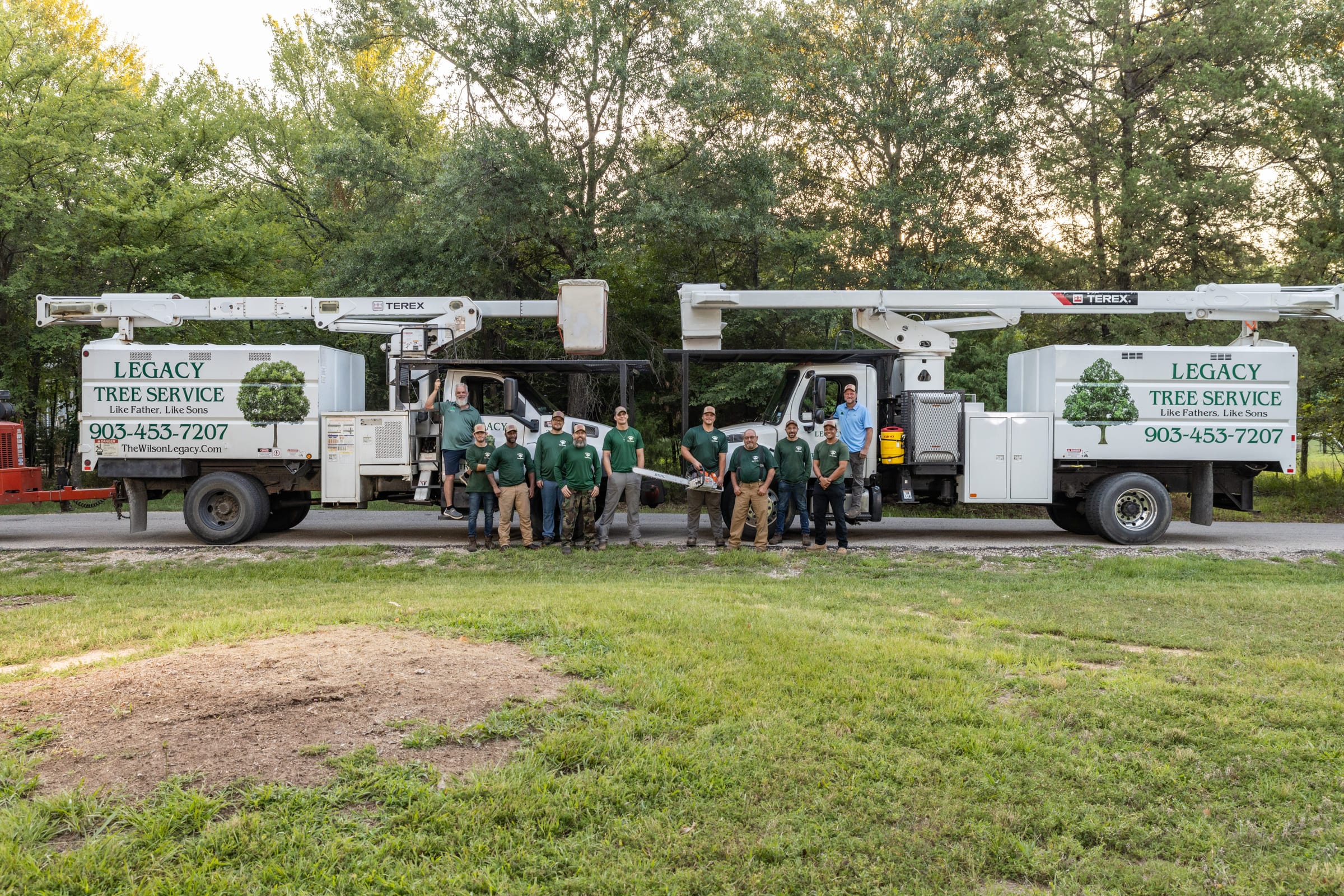 A tree-service crew standing in front of their line of branded bucket trucks on a cleared lot.