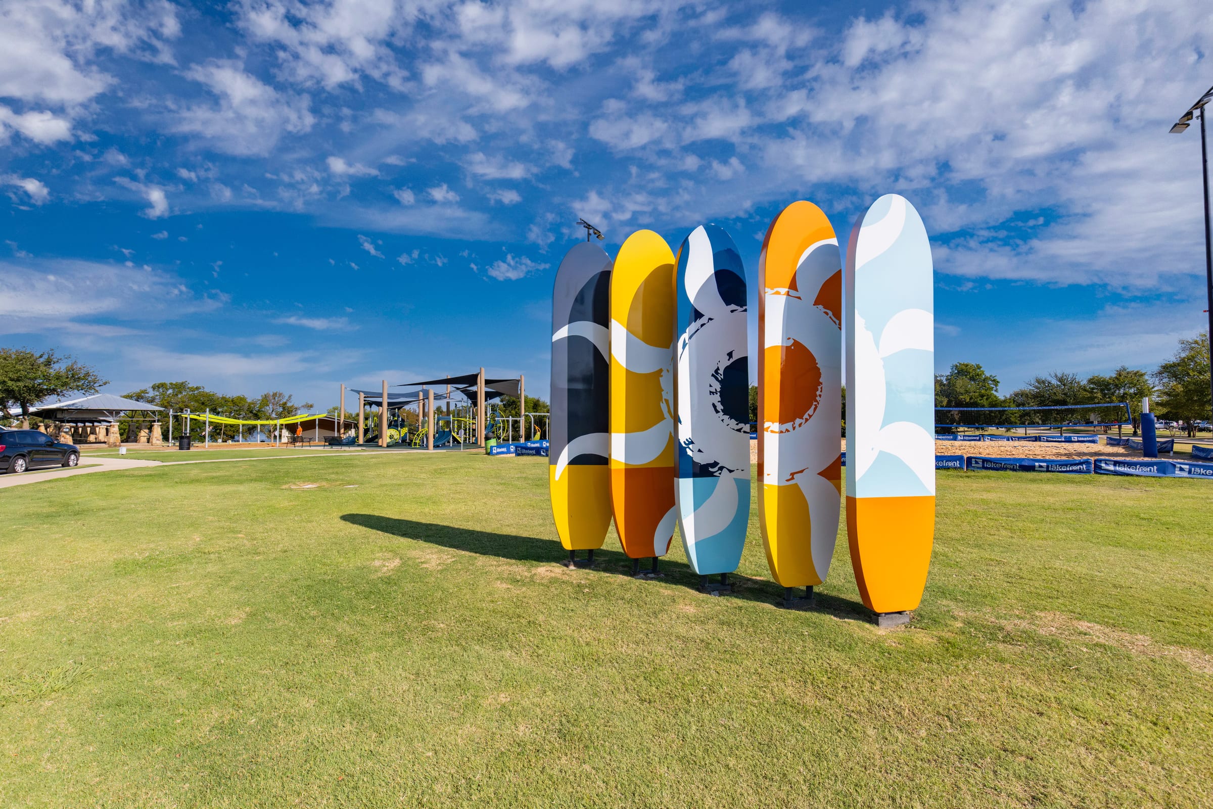 A row of tall painted sculptures standing on a mown green under a bright sky.