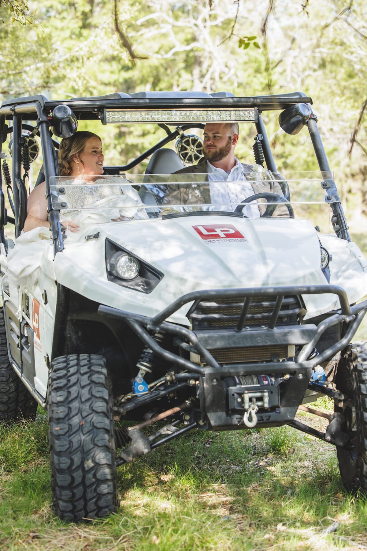 Two riders in a side-by-side utility vehicle on a wooded trail.