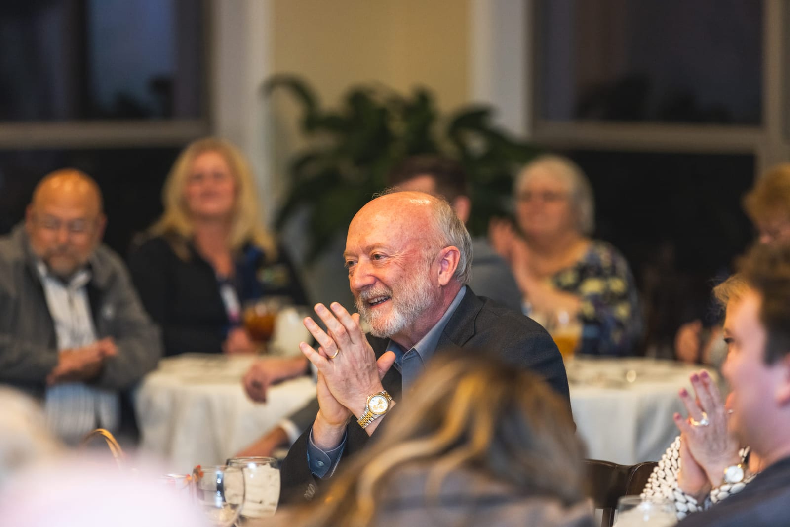 Banquet guests applauding at their table, one man leaning forward mid-clap.