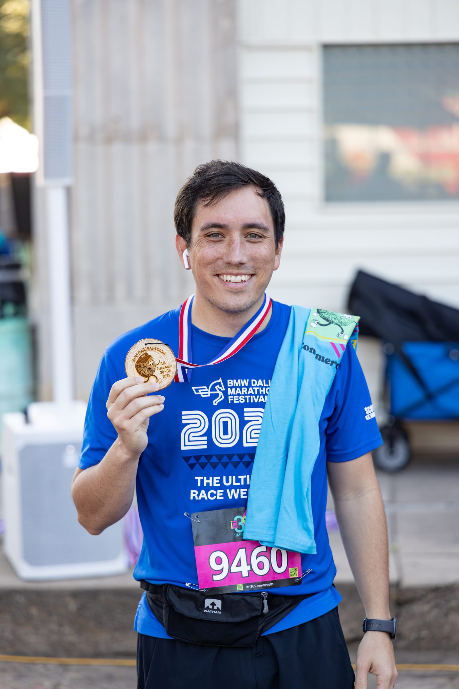 A runner holding out his finisher medal after a road race, bib still pinned on.