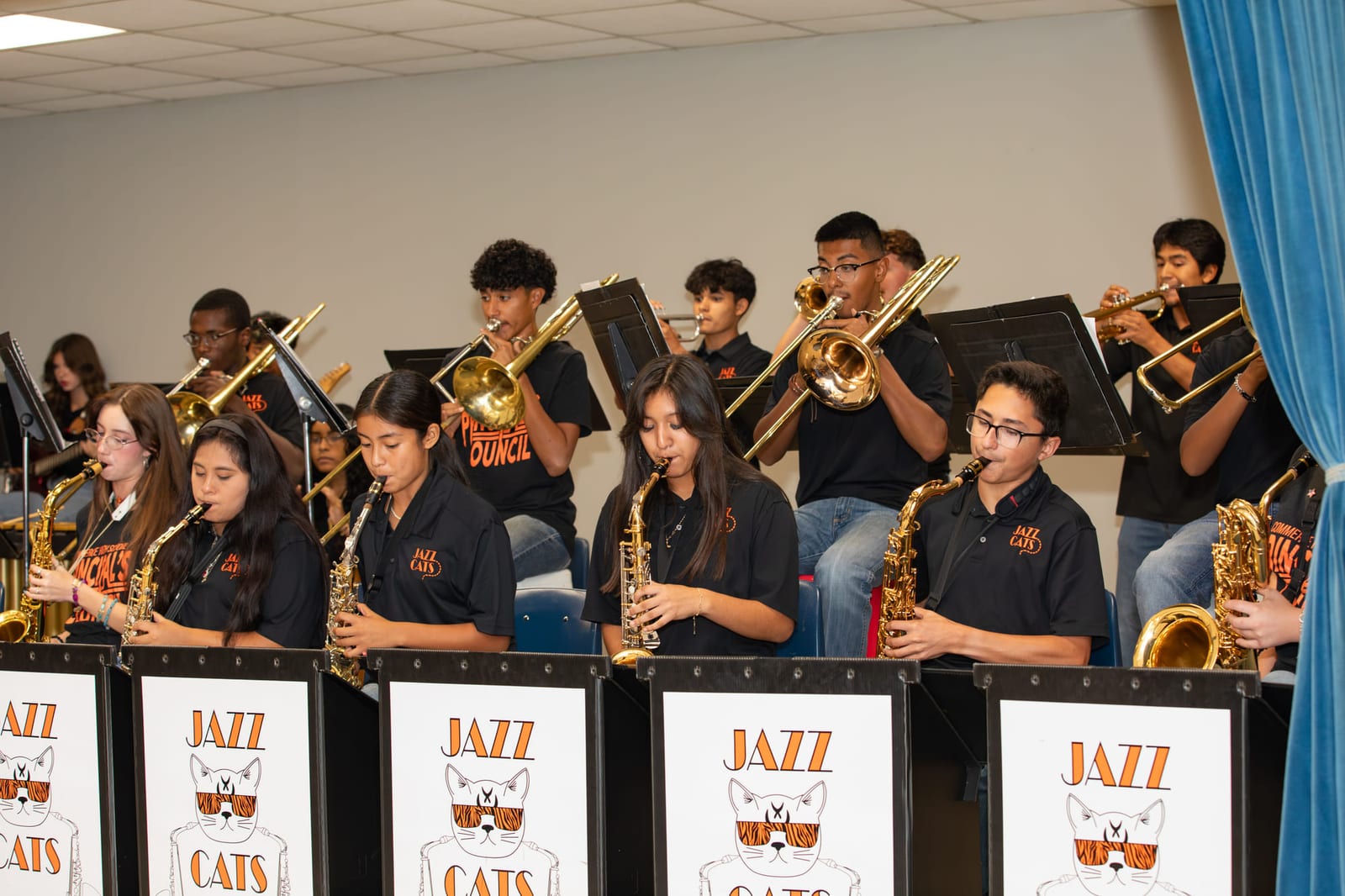 A school jazz band mid-performance, the brass section raised behind lettered stands.
