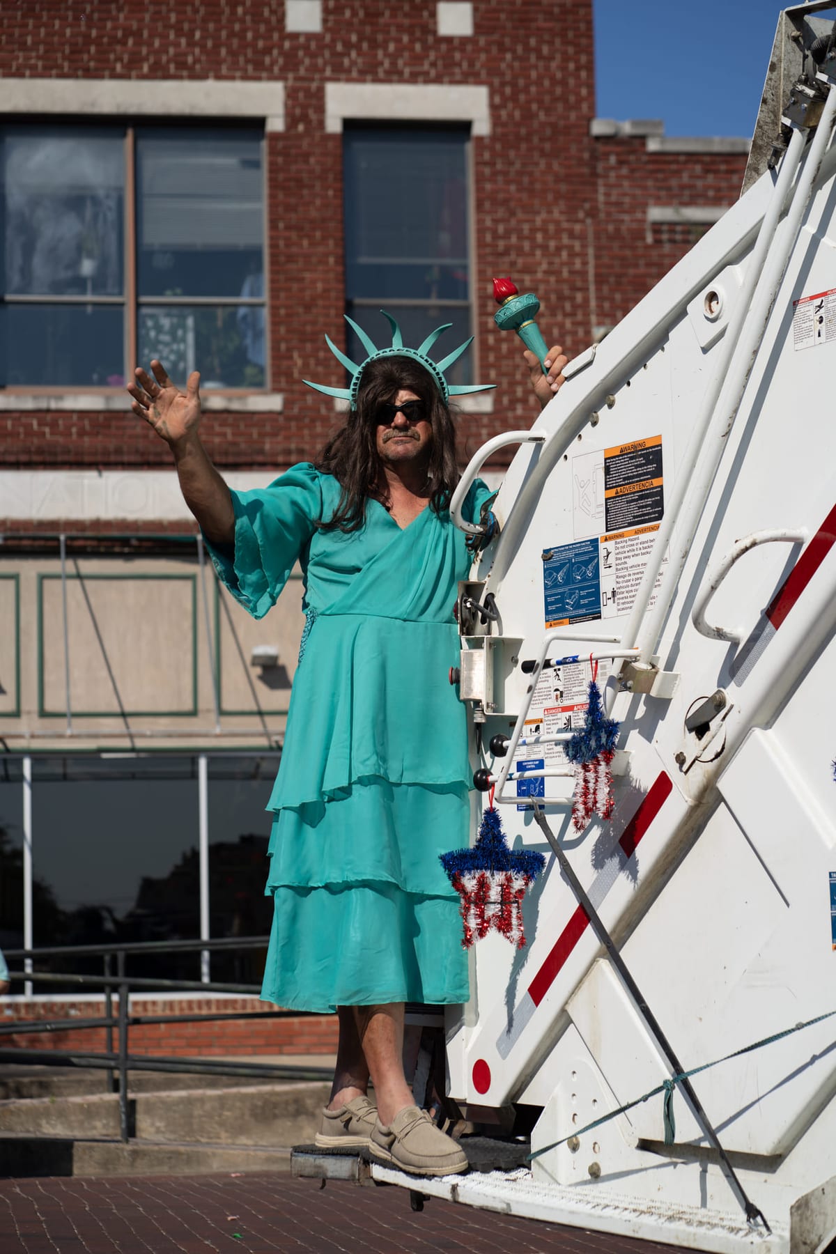 A parade performer costumed as the Statue of Liberty riding a lift truck down a brick street.