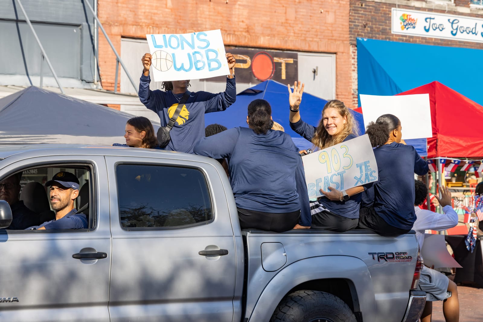 Supporters riding in the bed of a pickup during a downtown parade, hand-lettered signs held up.