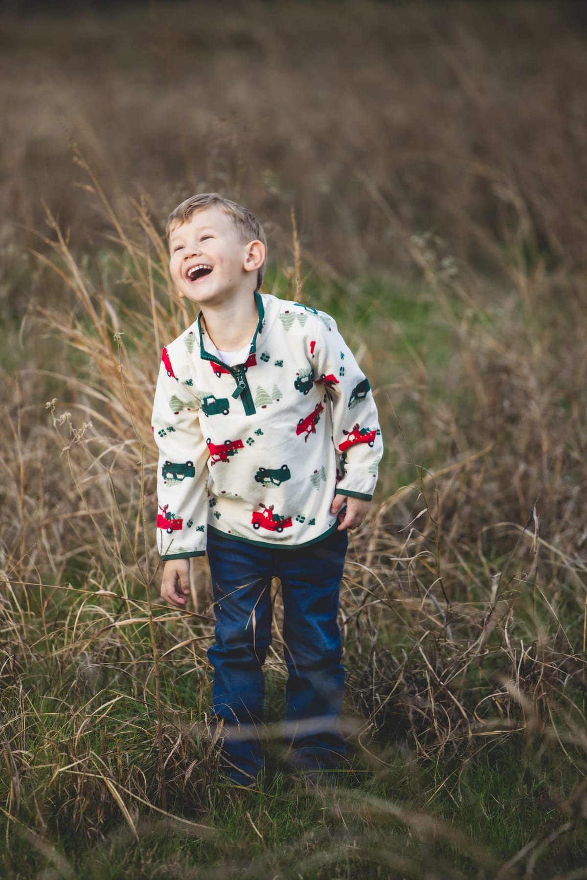 A boy laughing mid-step in waist-high winter grass, late sun behind him.