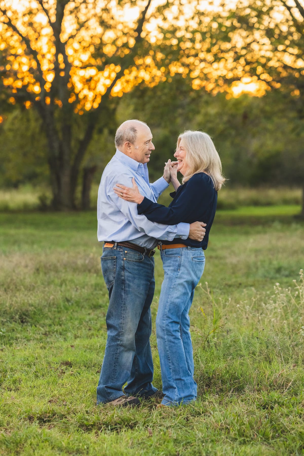 An older couple dancing together in an open field at golden hour.