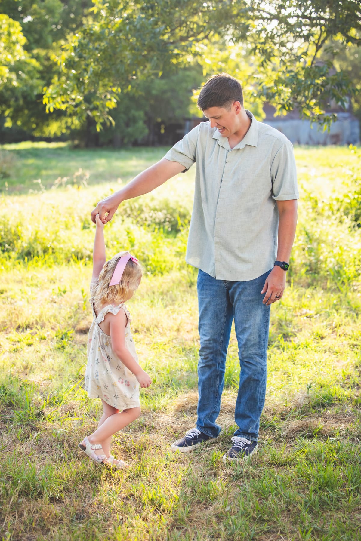 A father turning his young daughter by the hand in a mown field.