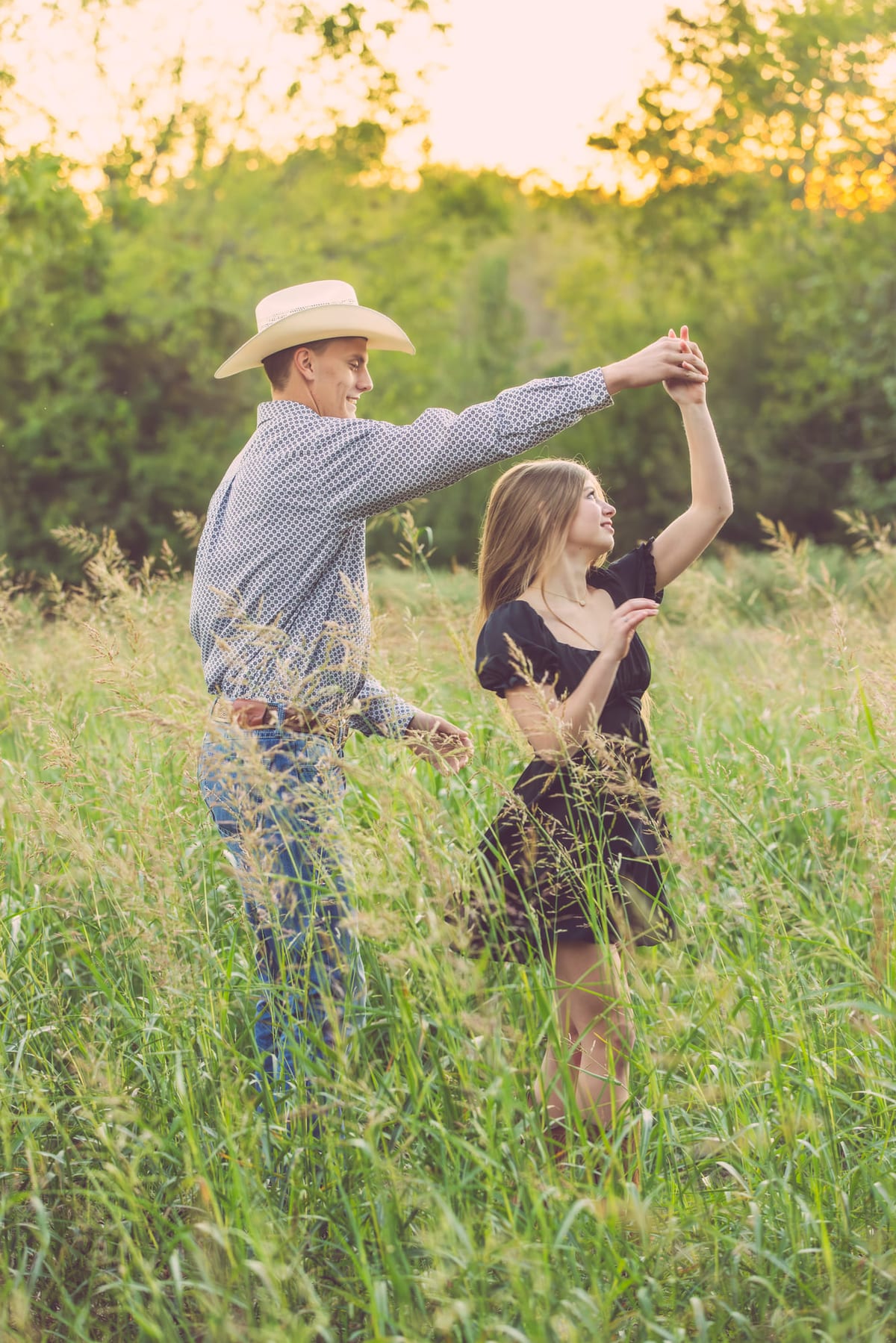 A father turning his daughter under his arm in tall grass, both mid-step.
