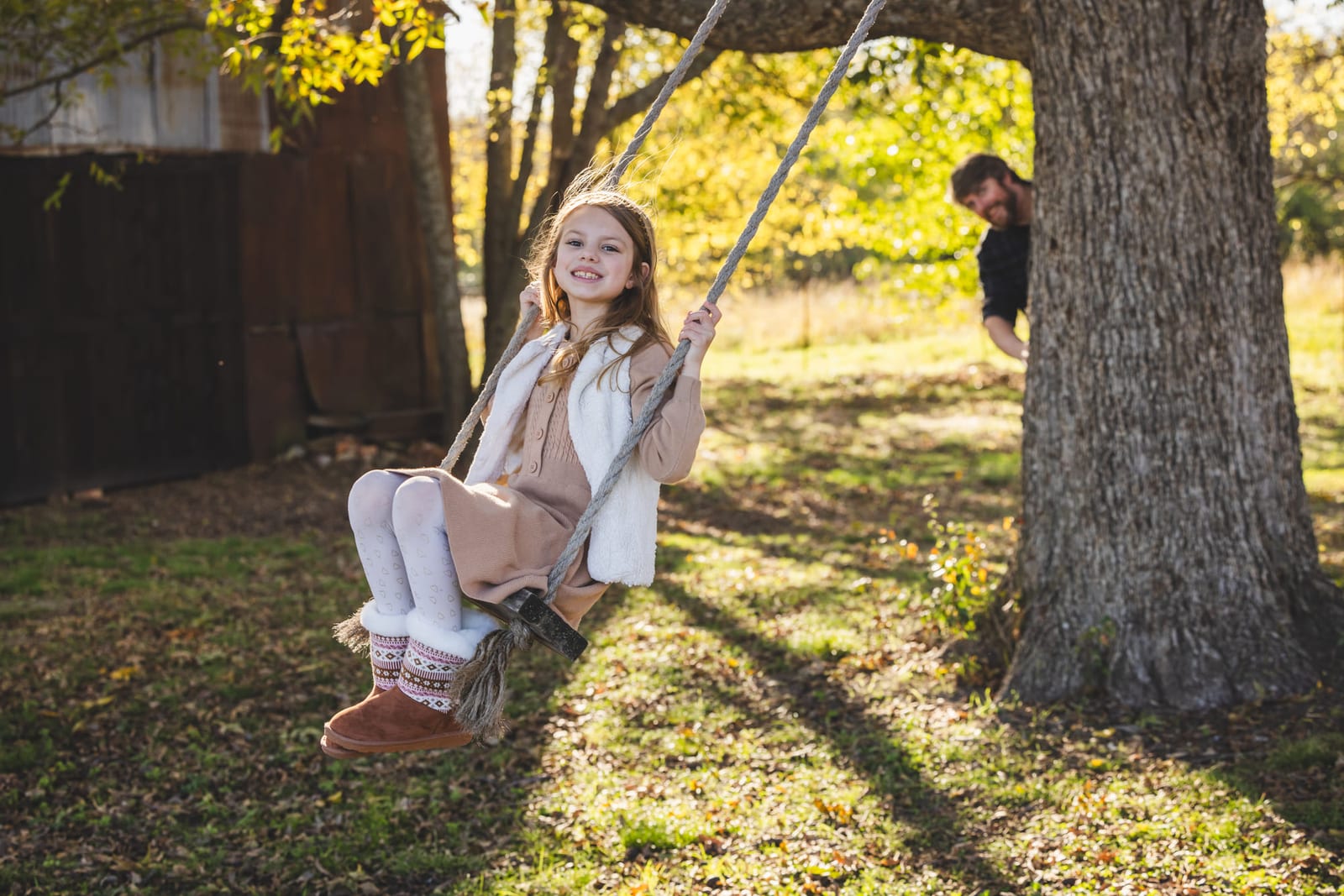 A girl on a rope swing under a big tree, dappled light across the grass.