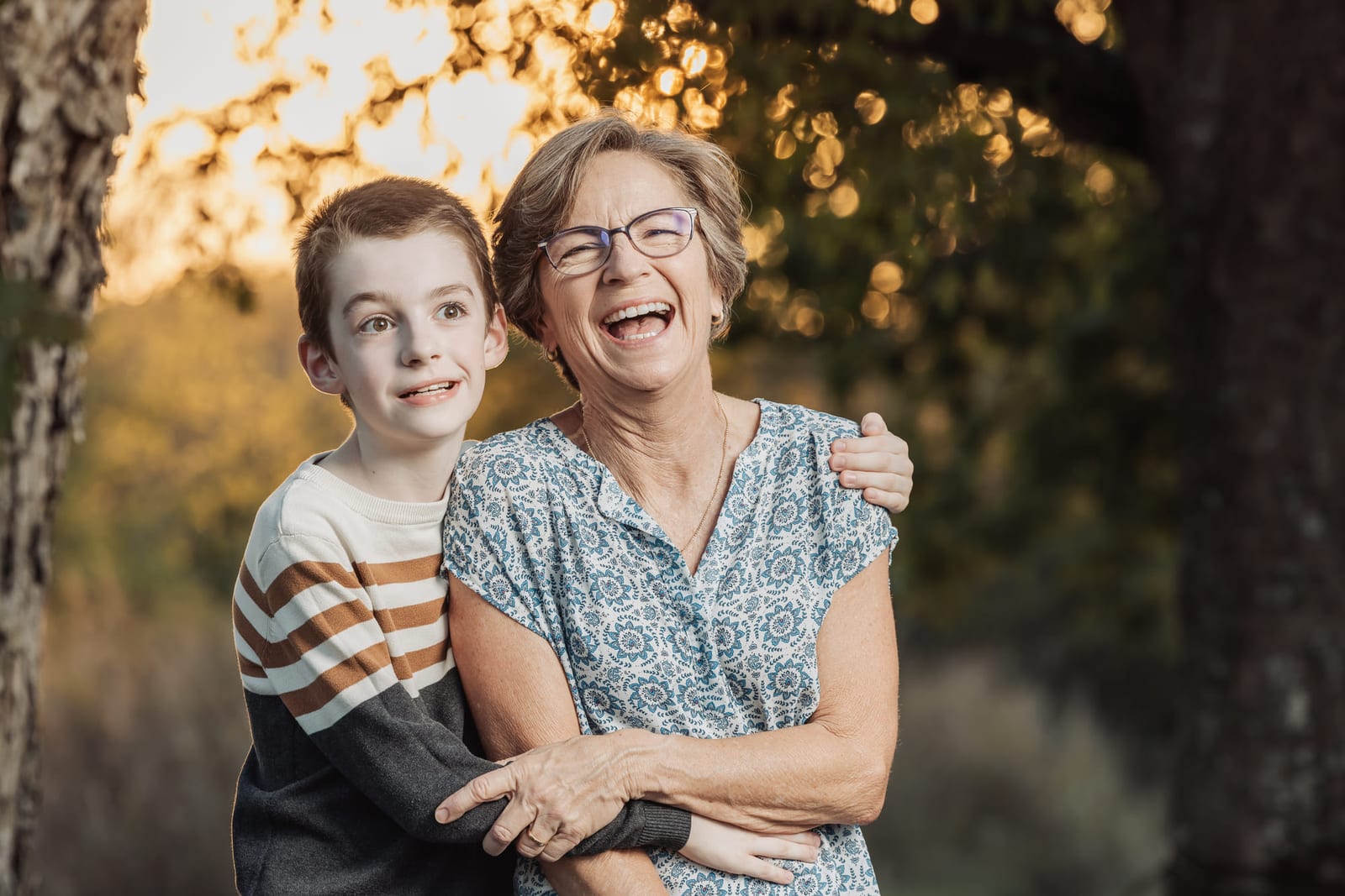 A grandmother laughing with her grandson leaning into her, backlit by low sun.