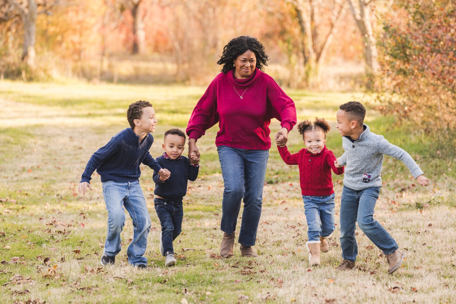 A mother running down a grass track holding hands with four children.