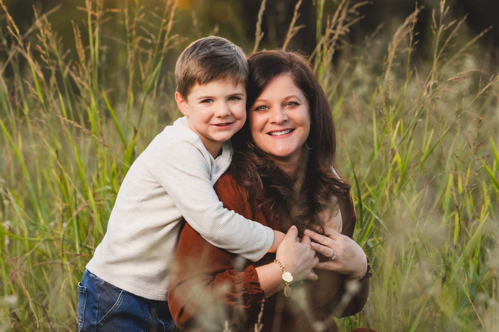 A small boy with his arms wrapped around his mother in tall grass, both laughing.