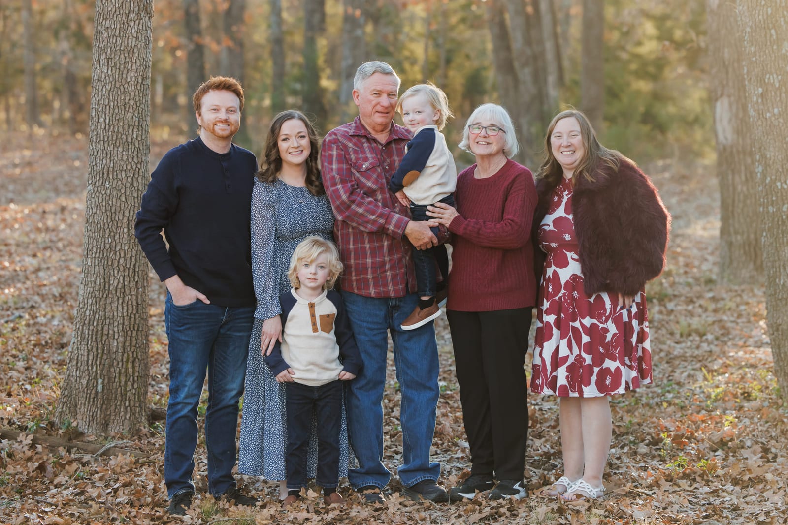 Three generations lined up in autumn woods, the youngest carried on a hip at the centre.