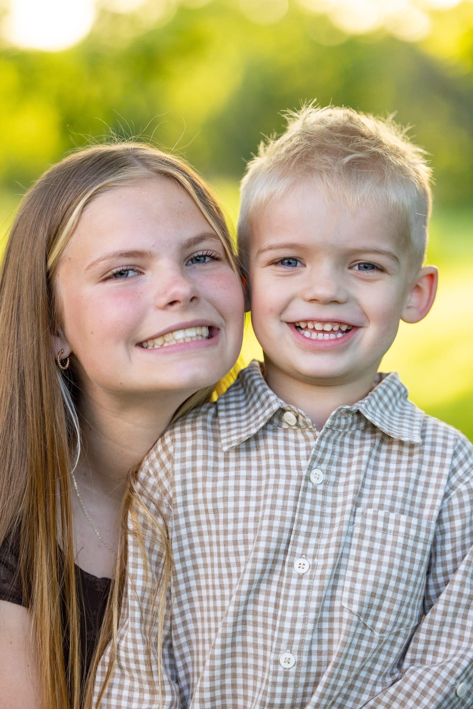 Two siblings cheek to cheek in the open, both grinning straight into the lens.