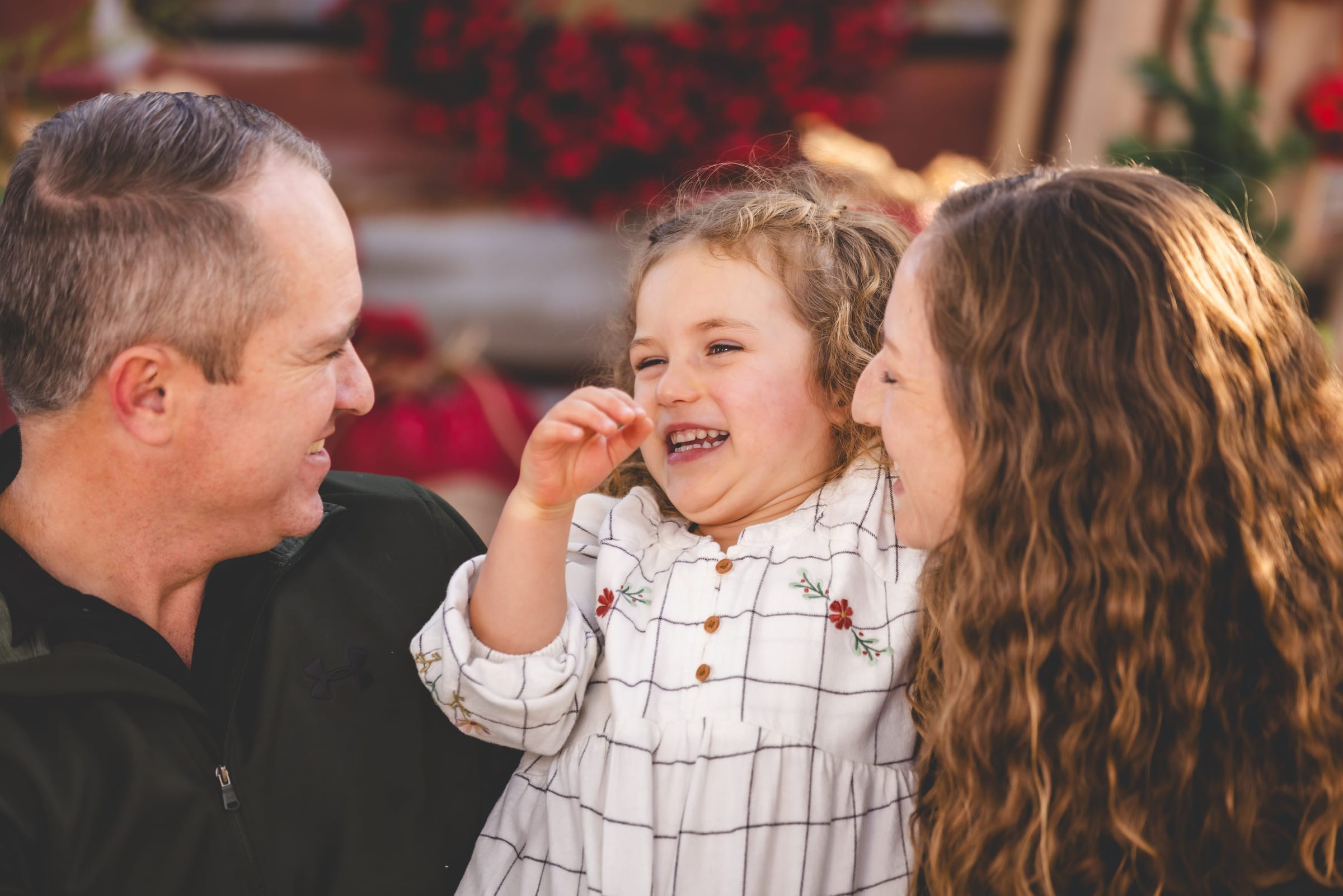 A father, mother and daughter laughing together in close, the child mid-word between them.