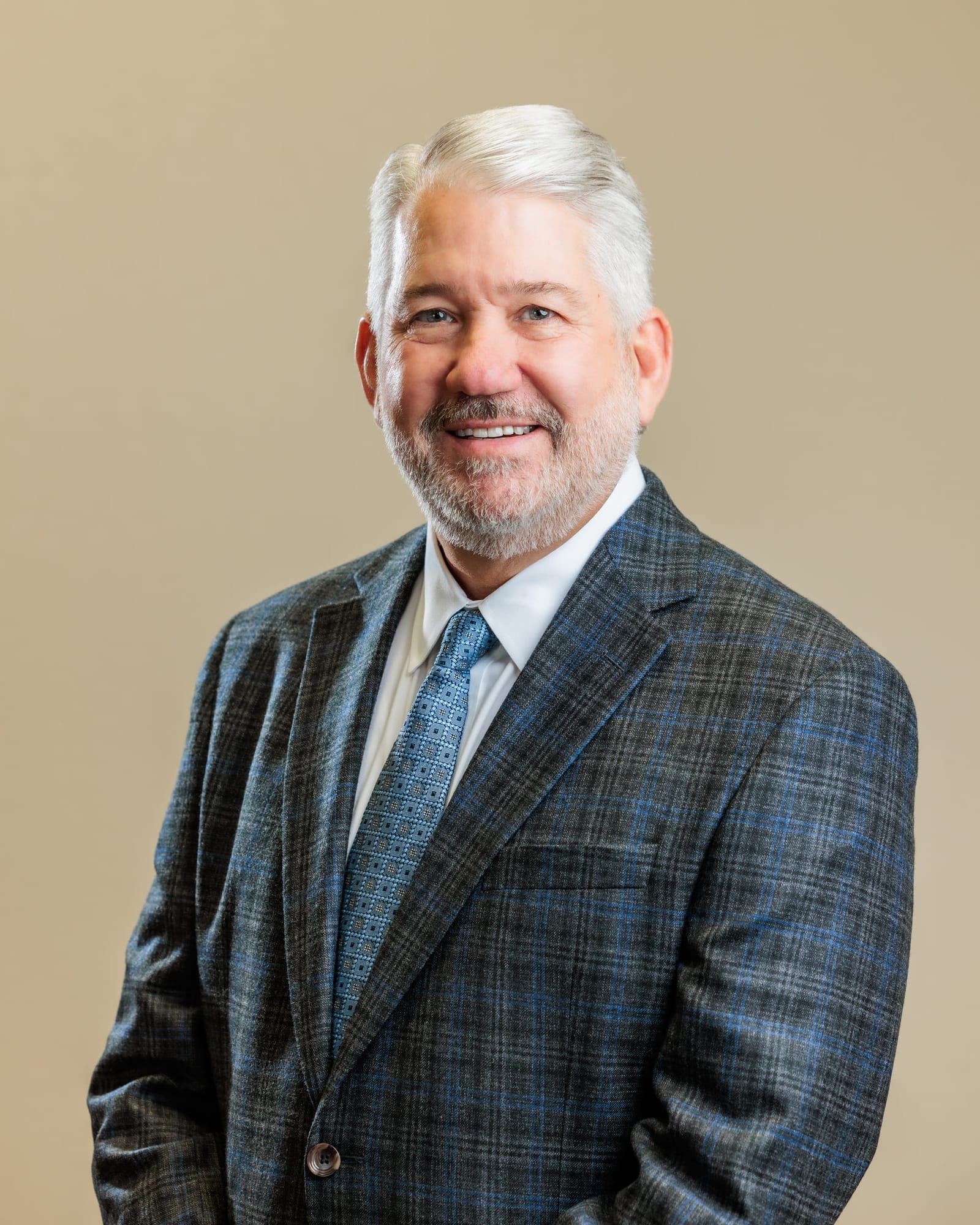 Business portrait of a man in a checked jacket and tie against a warm neutral wall.
