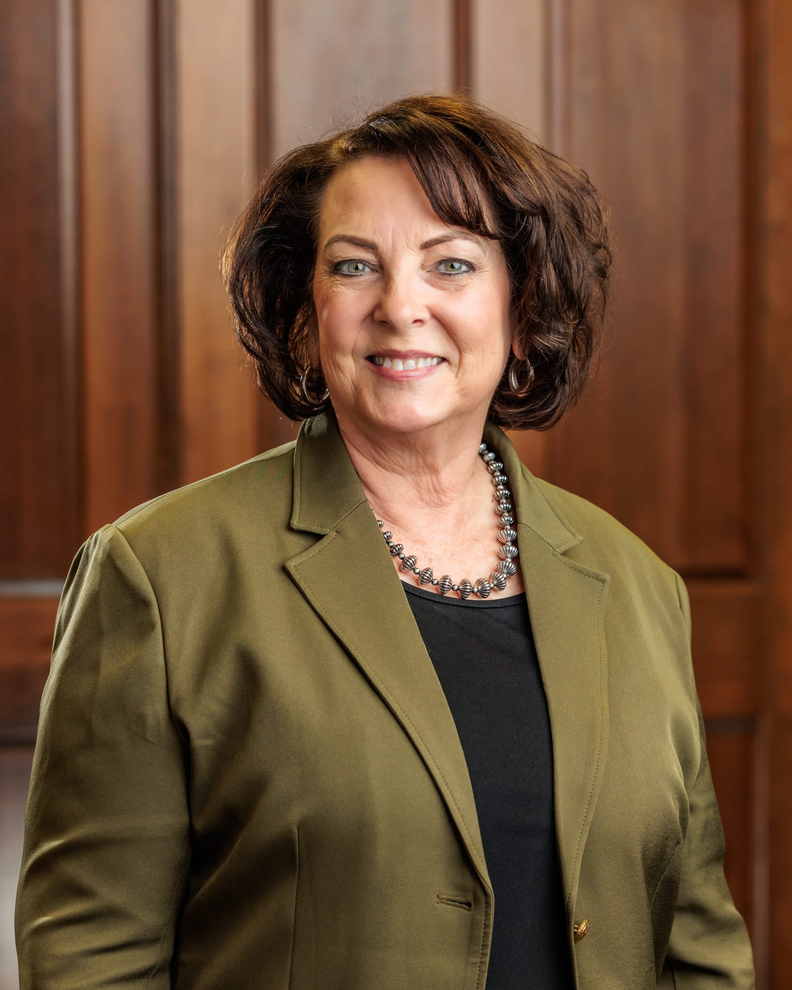 Business portrait of a woman in an olive blazer standing in front of a dark wood door.