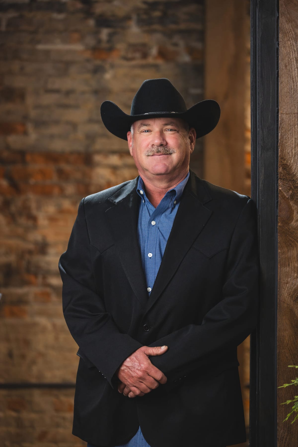 A studio portrait in a black cowboy hat and dark jacket against brick.