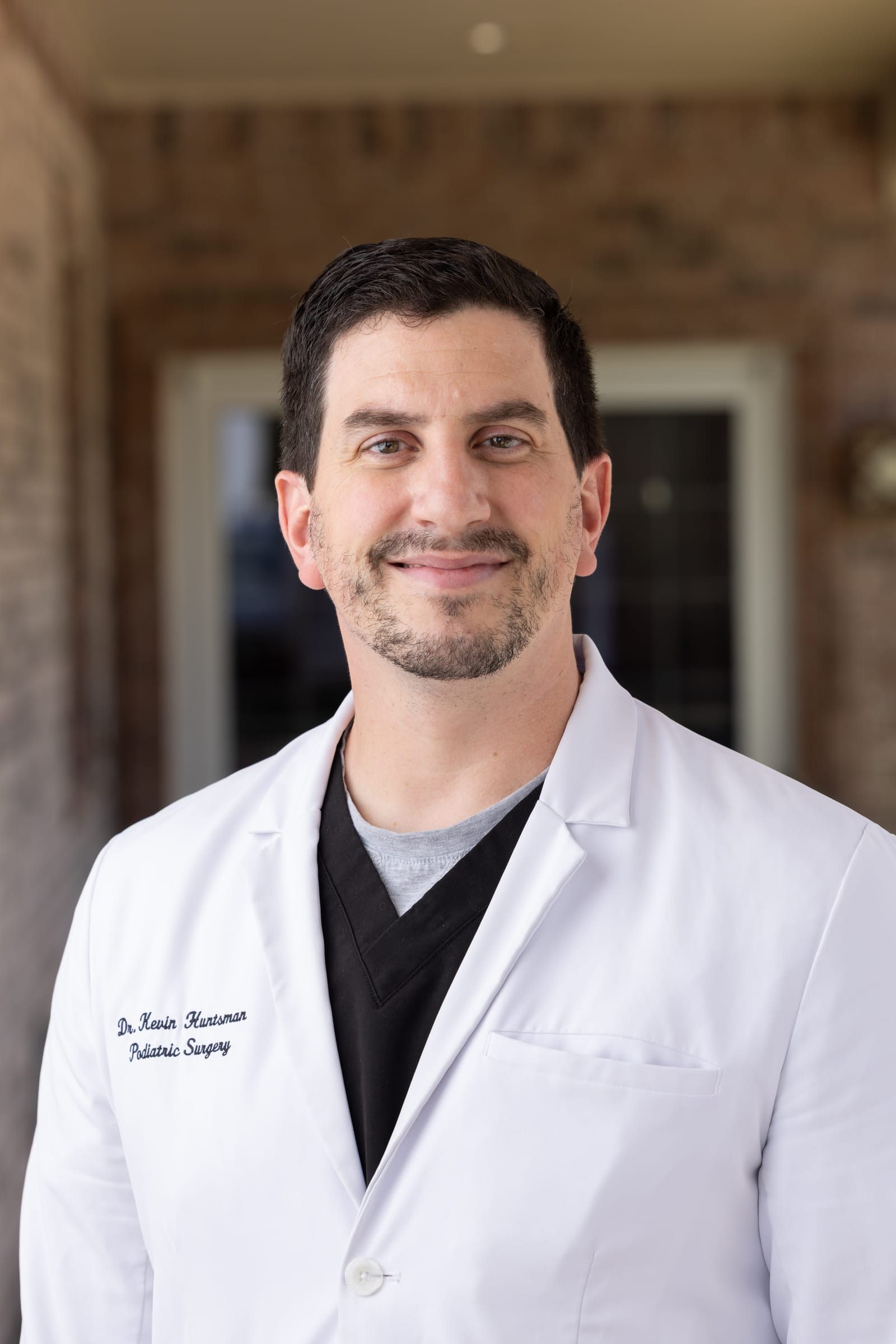 A physician in a white coat photographed on a brick porch.