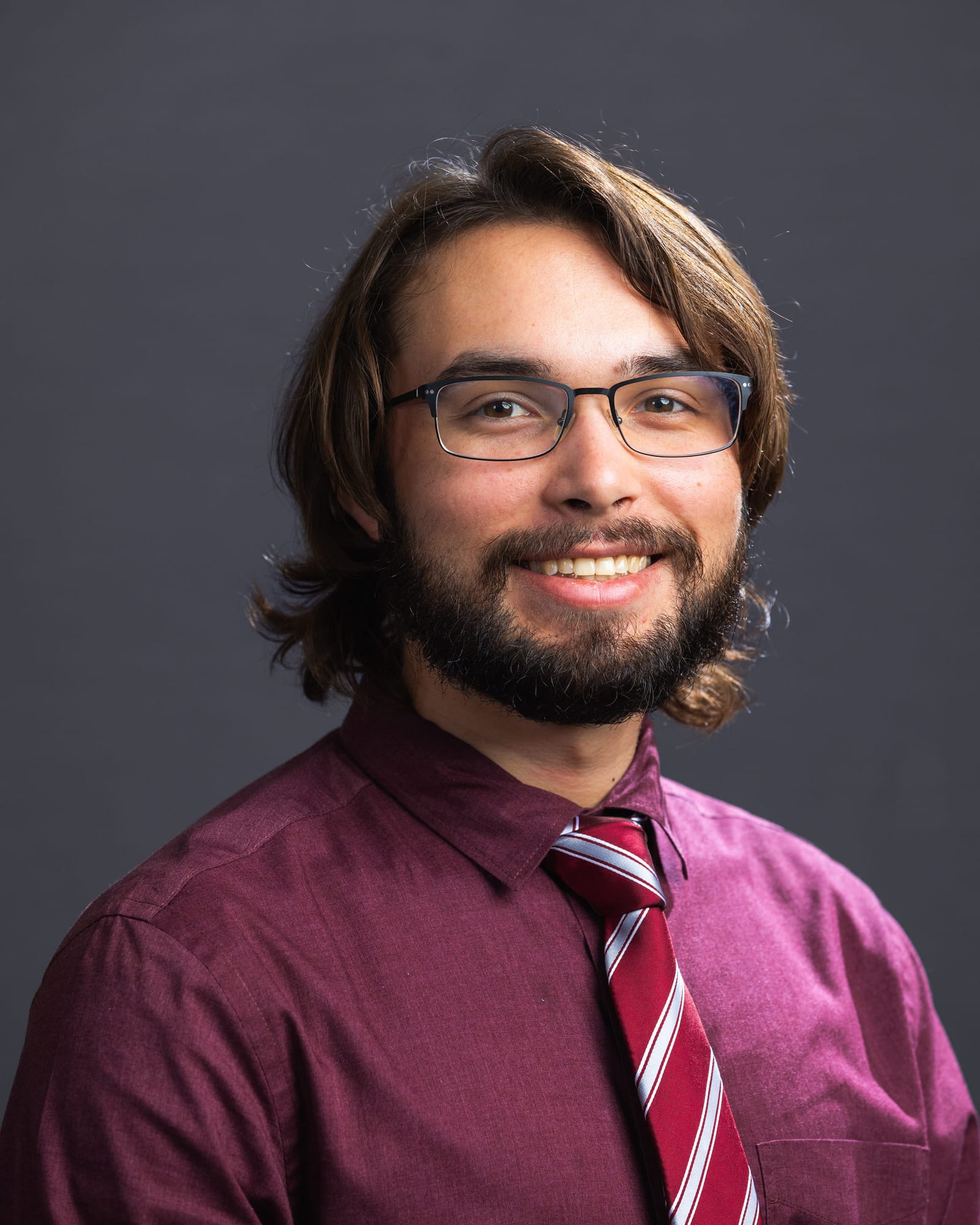 A studio headshot in glasses and a striped tie against a plain grey backdrop.