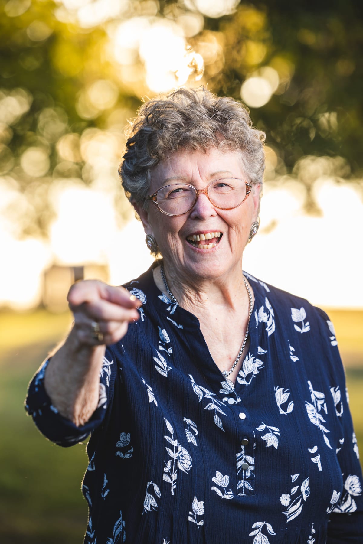 A portrait outdoors of someone laughing and pointing straight at the camera.