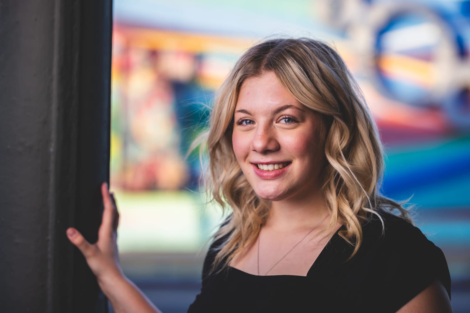 A portrait in front of a painted mural, one hand open mid-gesture.