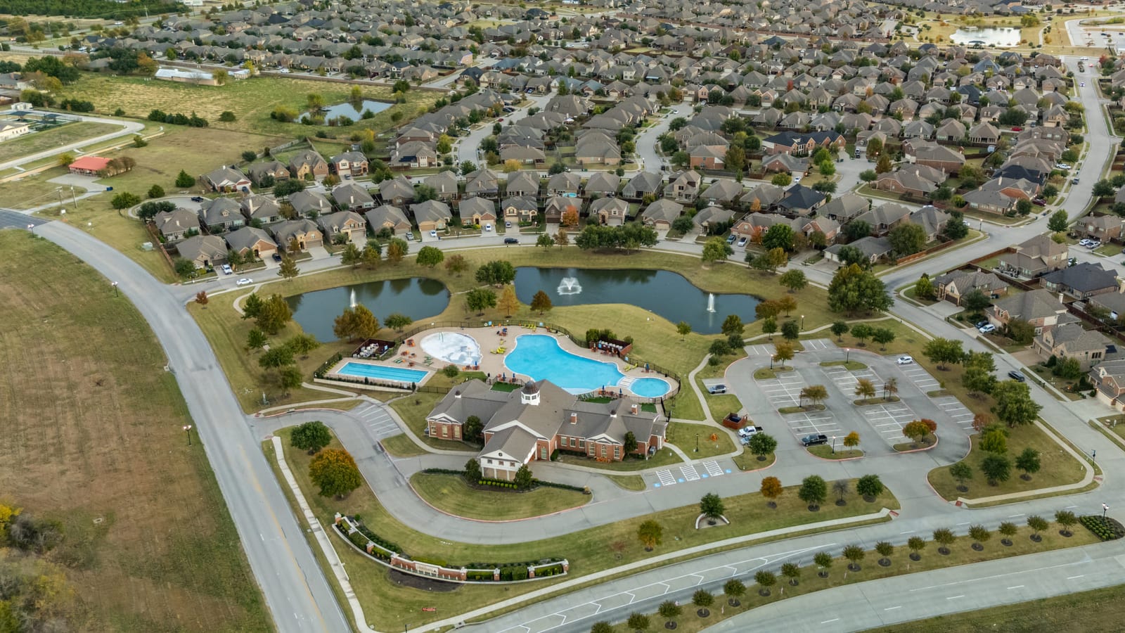 Aerial view of a master-planned neighbourhood, its amenity centre and resort-style pool ringed by curving streets and young trees.
