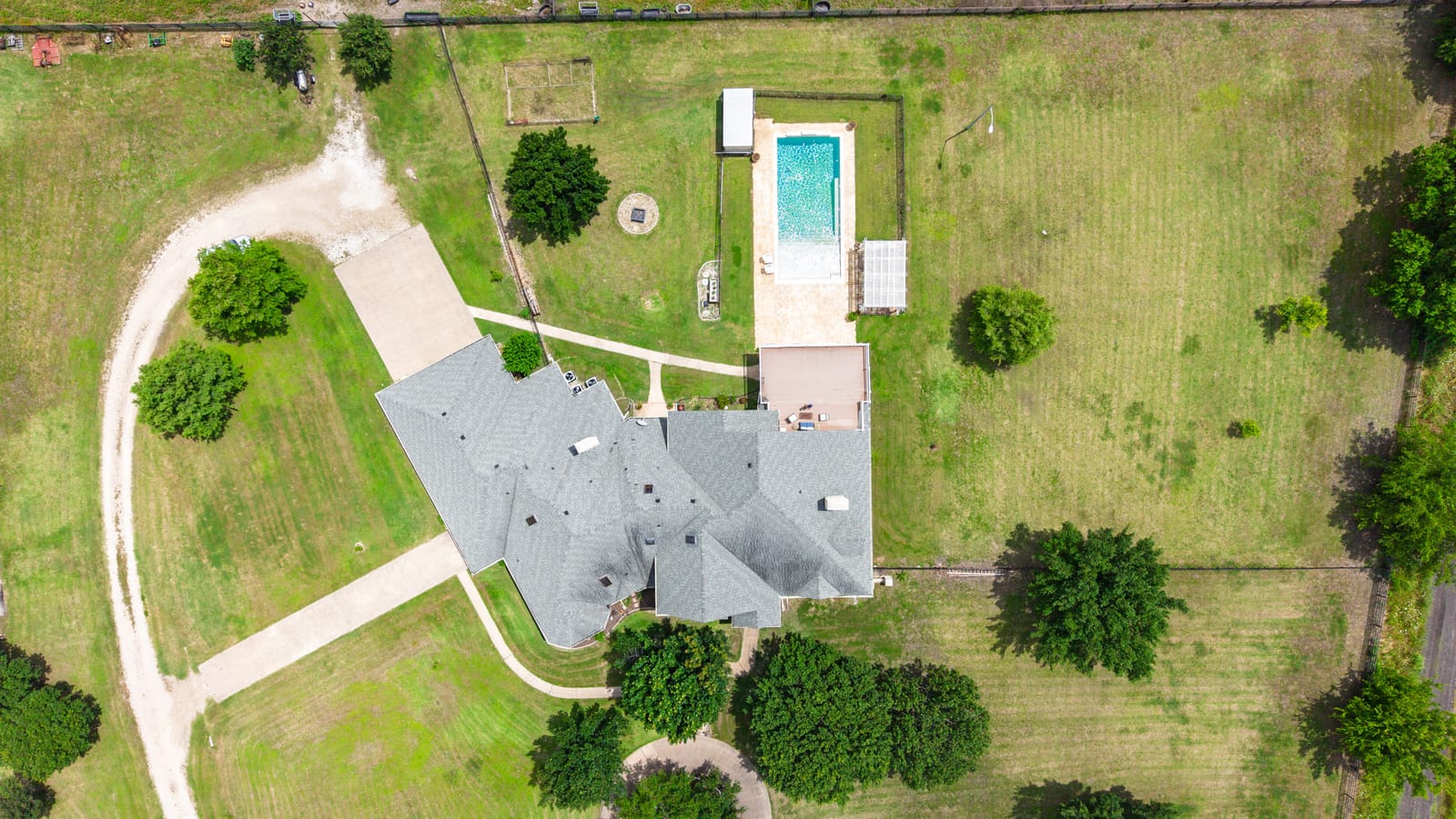 A top-down aerial of a house and its pool set in mown acreage, the drive curving in from the road.