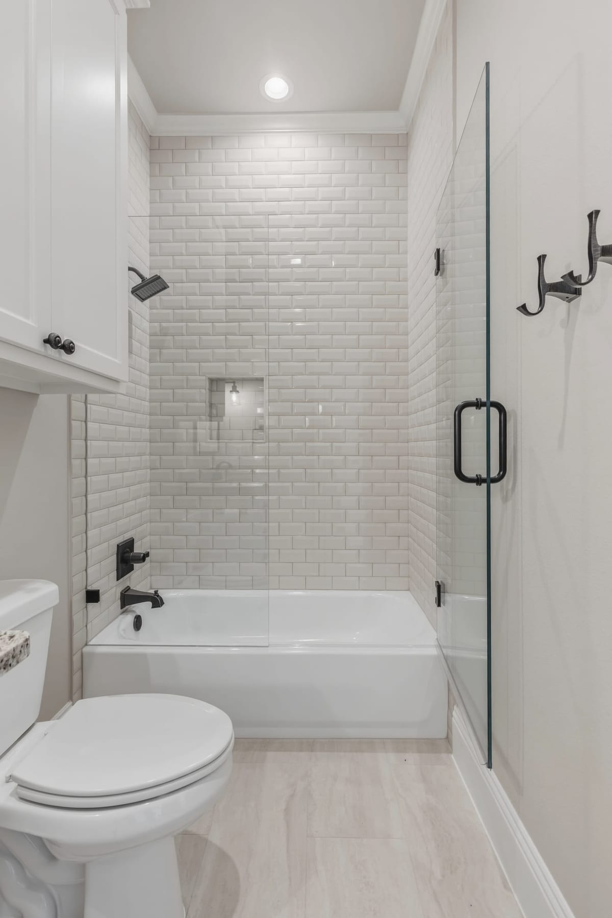 A full bath in white subway tile with a glass shower screen, matte-black fittings and a tiled tub surround.