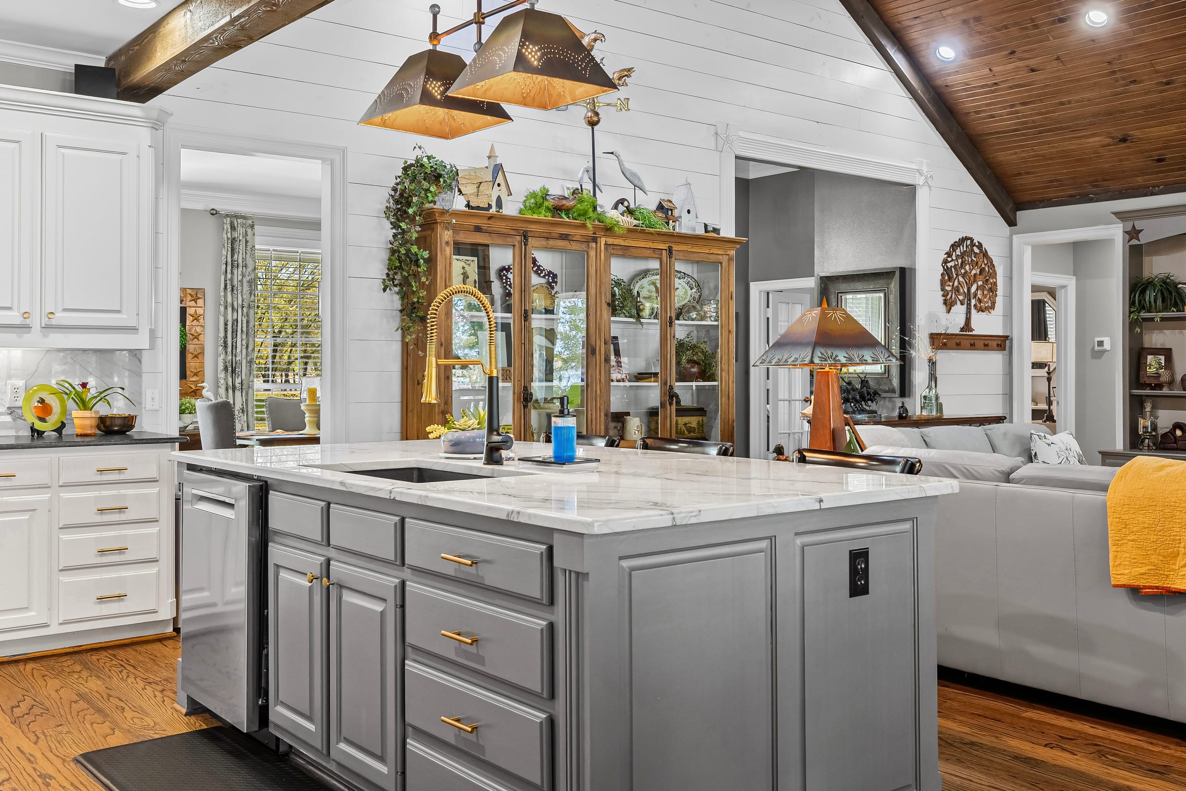A white kitchen under a vaulted plank ceiling, a marble-topped island beneath two hanging lamps.
