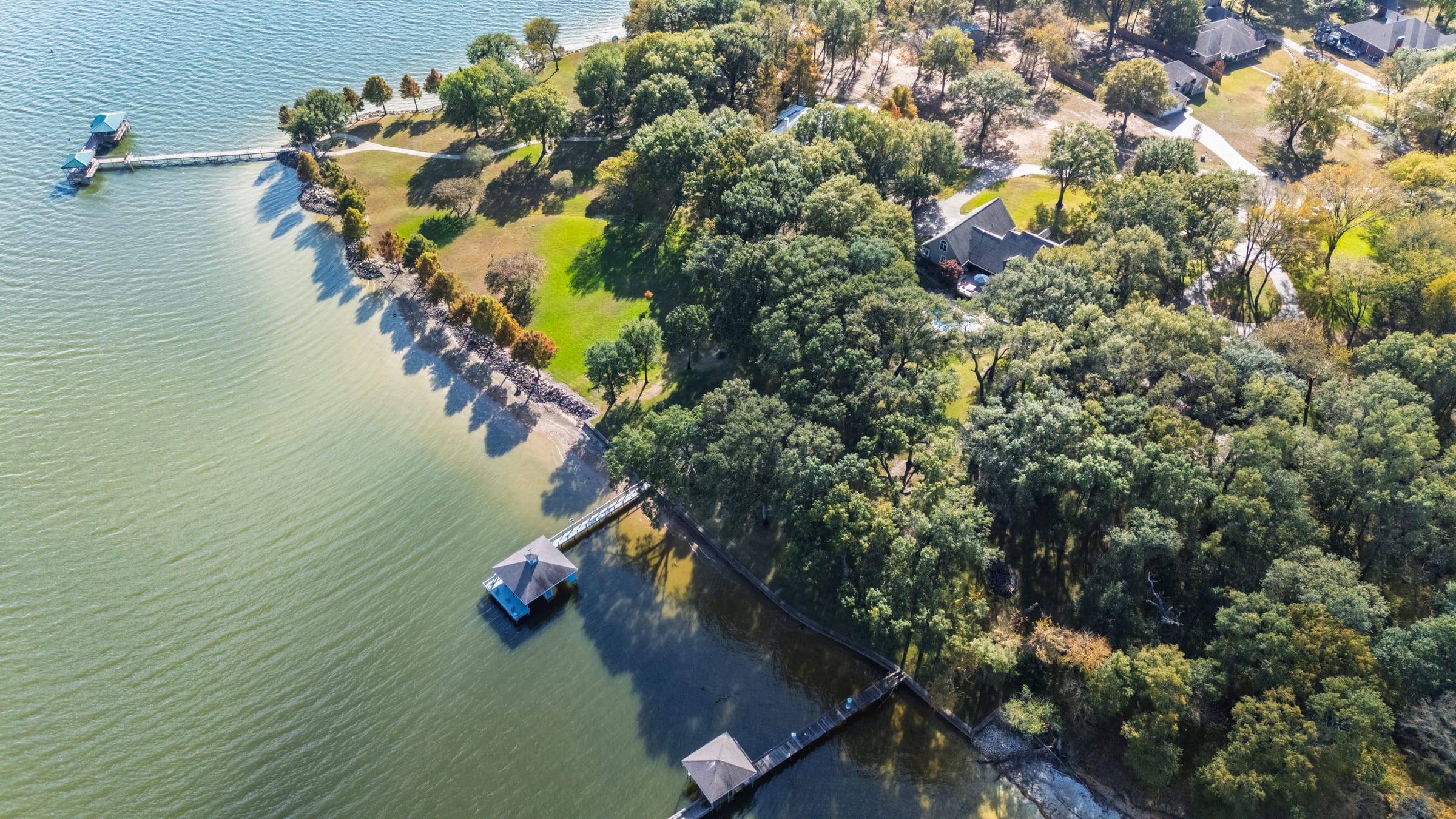 Aerial view of a wooded point on a lake, private docks stepping along the shoreline and open water beyond.