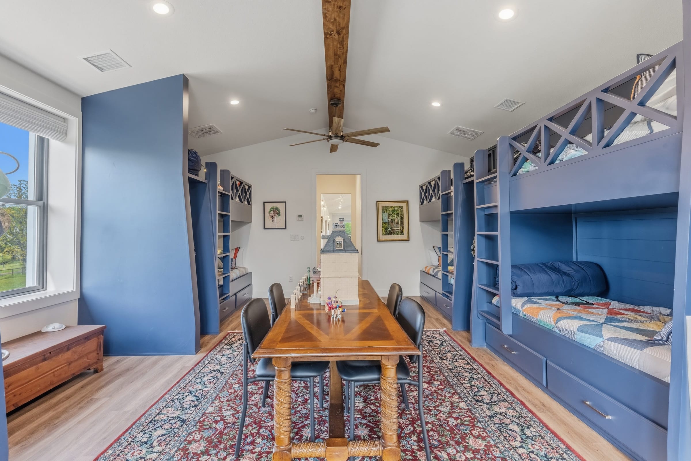 A bunk room painted deep blue, built-in bunks down both walls and a long table on a patterned rug between them.