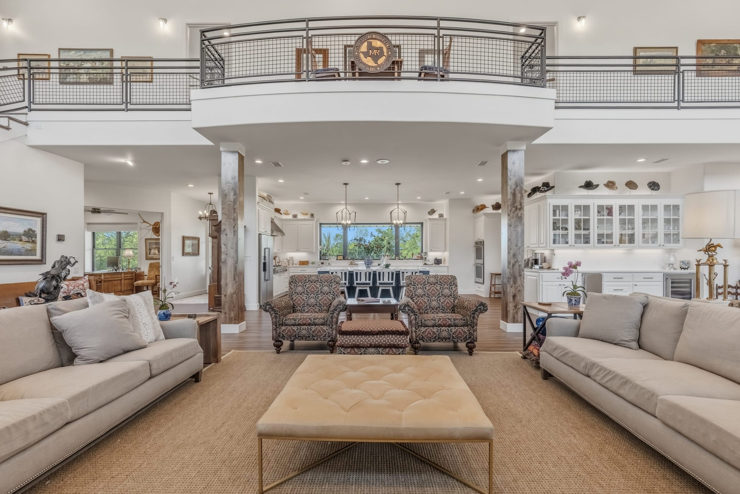 A double-height great room with a railed loft balcony above, two long sofas facing each other across a leather ottoman.