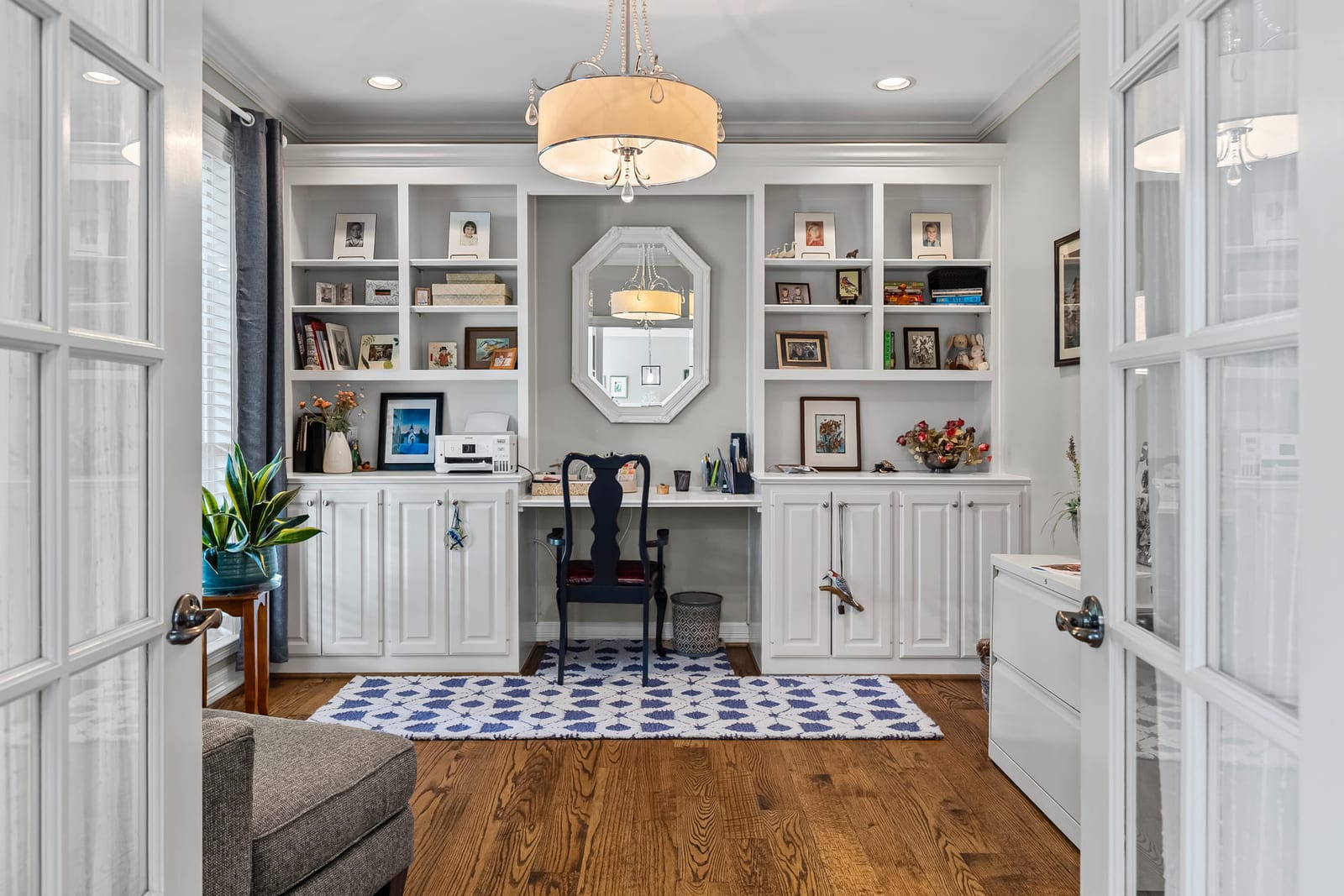A home study seen through open French doors, built-in shelving on three walls and a desk beneath an arched mirror.
