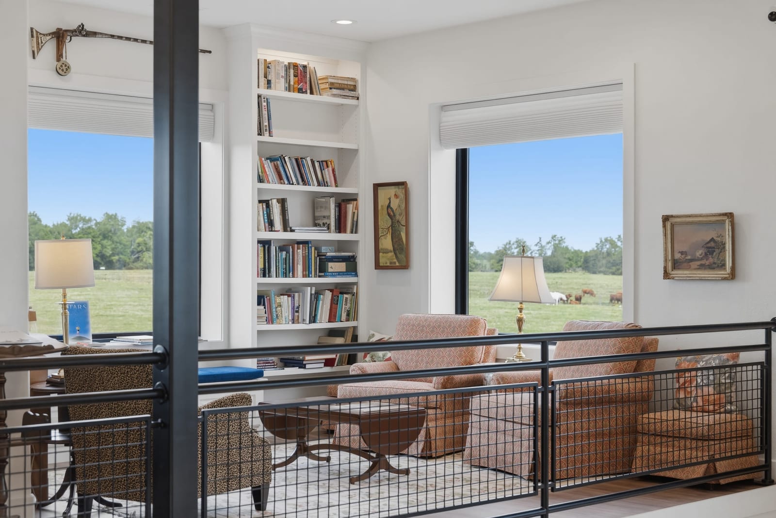 A study with floor-to-ceiling bookshelves and tall windows opening onto pasture.