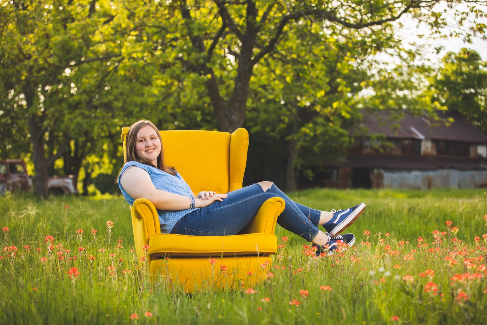 A senior reclining in a yellow wing chair set out in a field of red wildflowers.