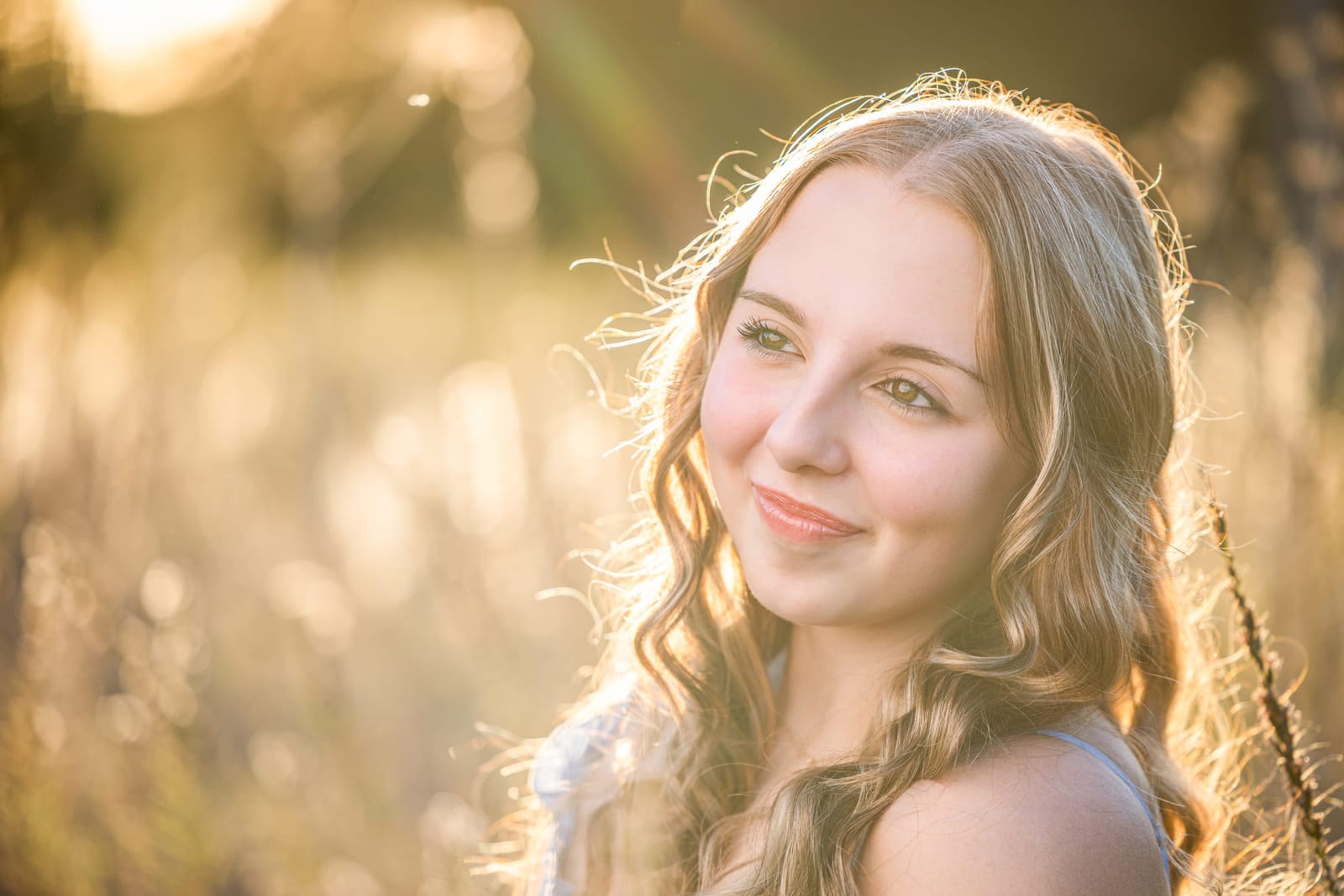 A senior portrait in tall grass at golden hour, the light coming through her hair from behind.
