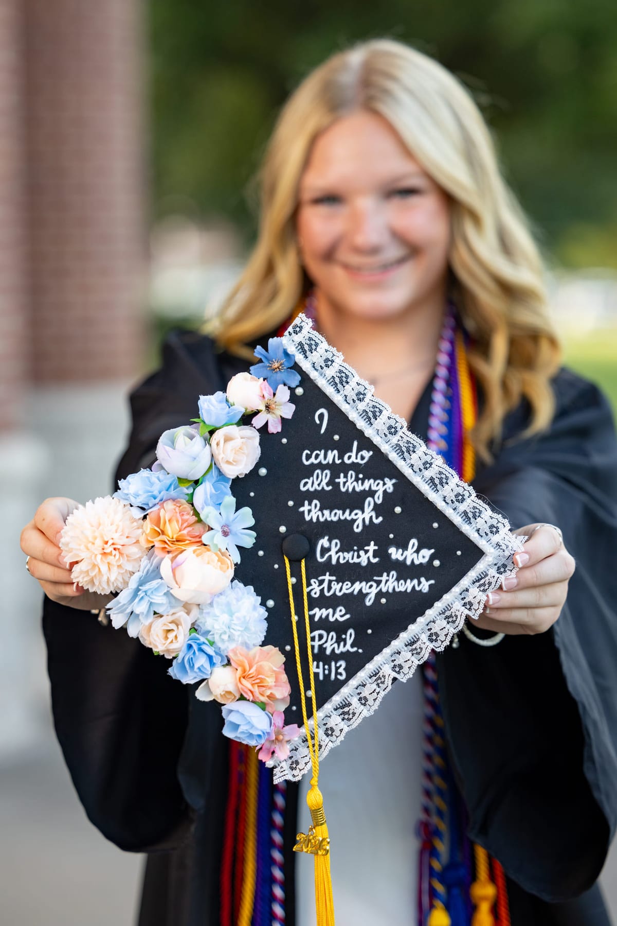 A graduate holding out a mortarboard decorated with lace and paper flowers.