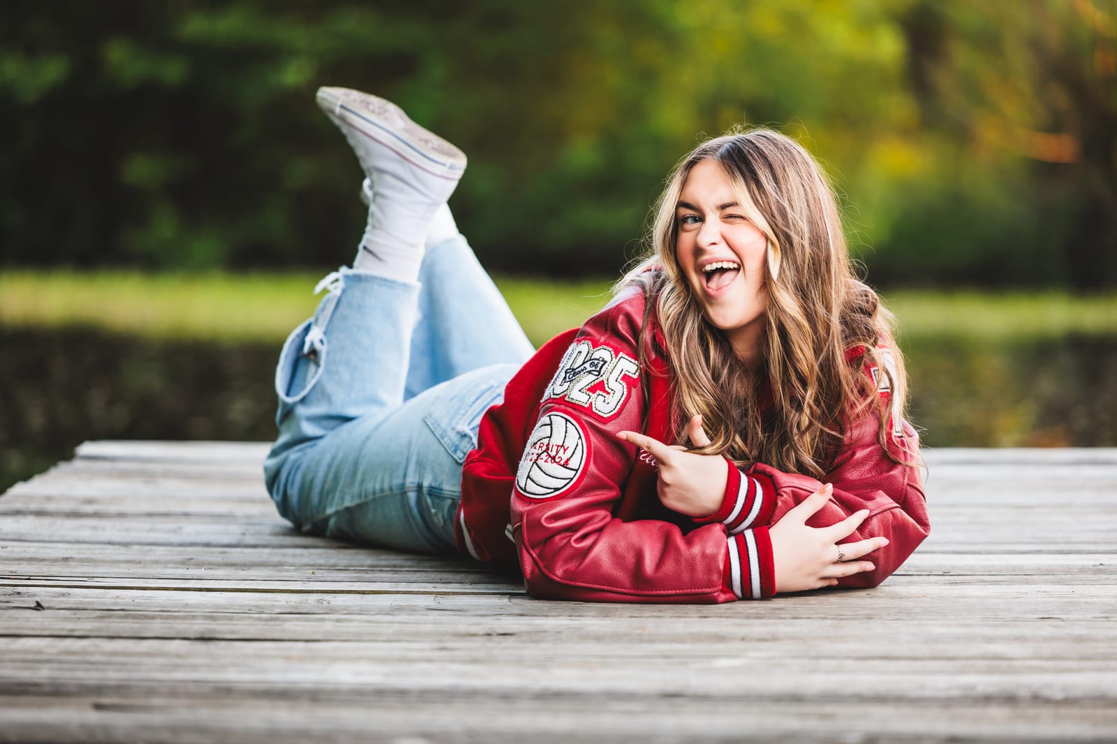 A senior lying on a dock in a letterman jacket, ankles crossed in the air.