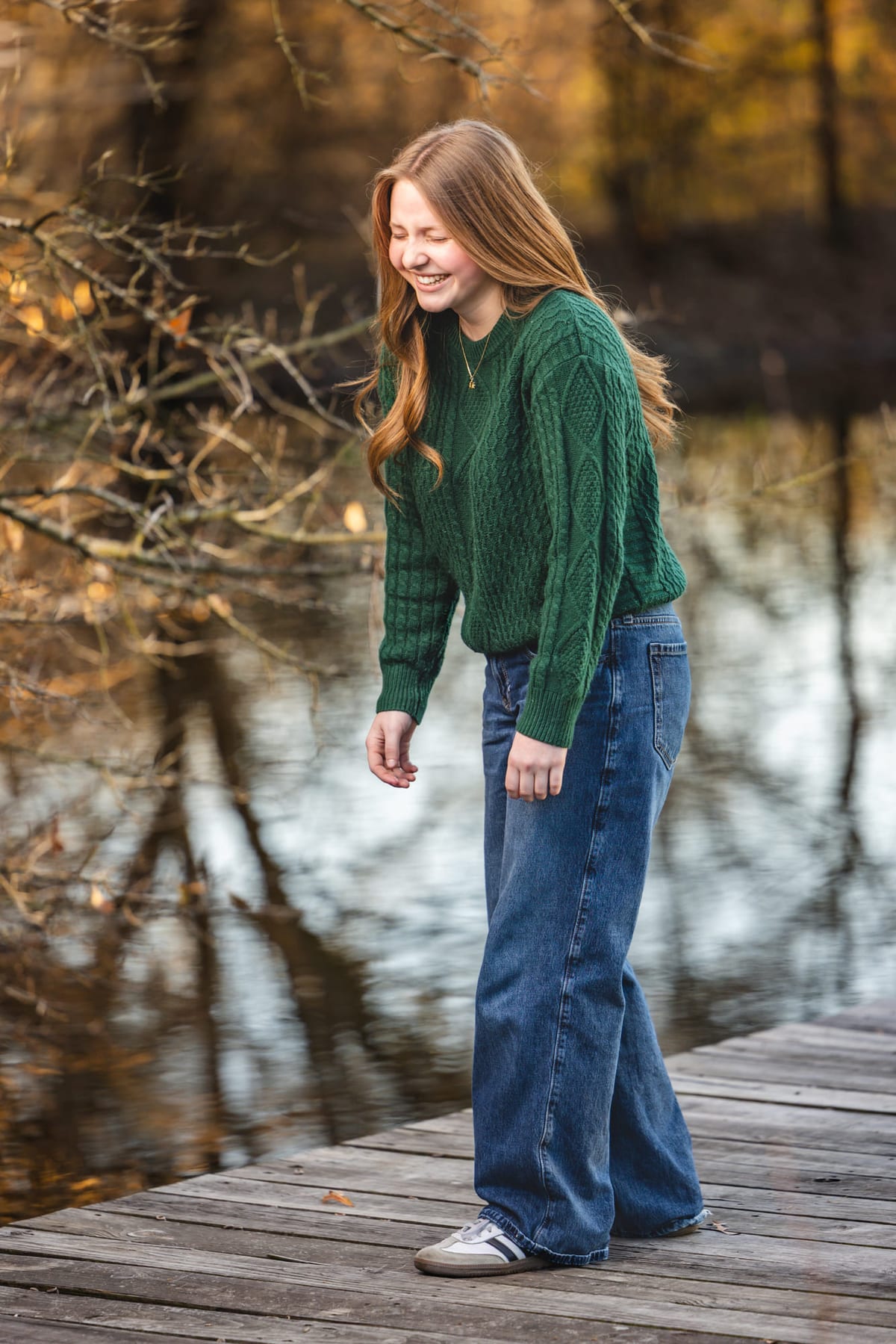A senior walking the length of a wooden dock, water and bare trees behind.