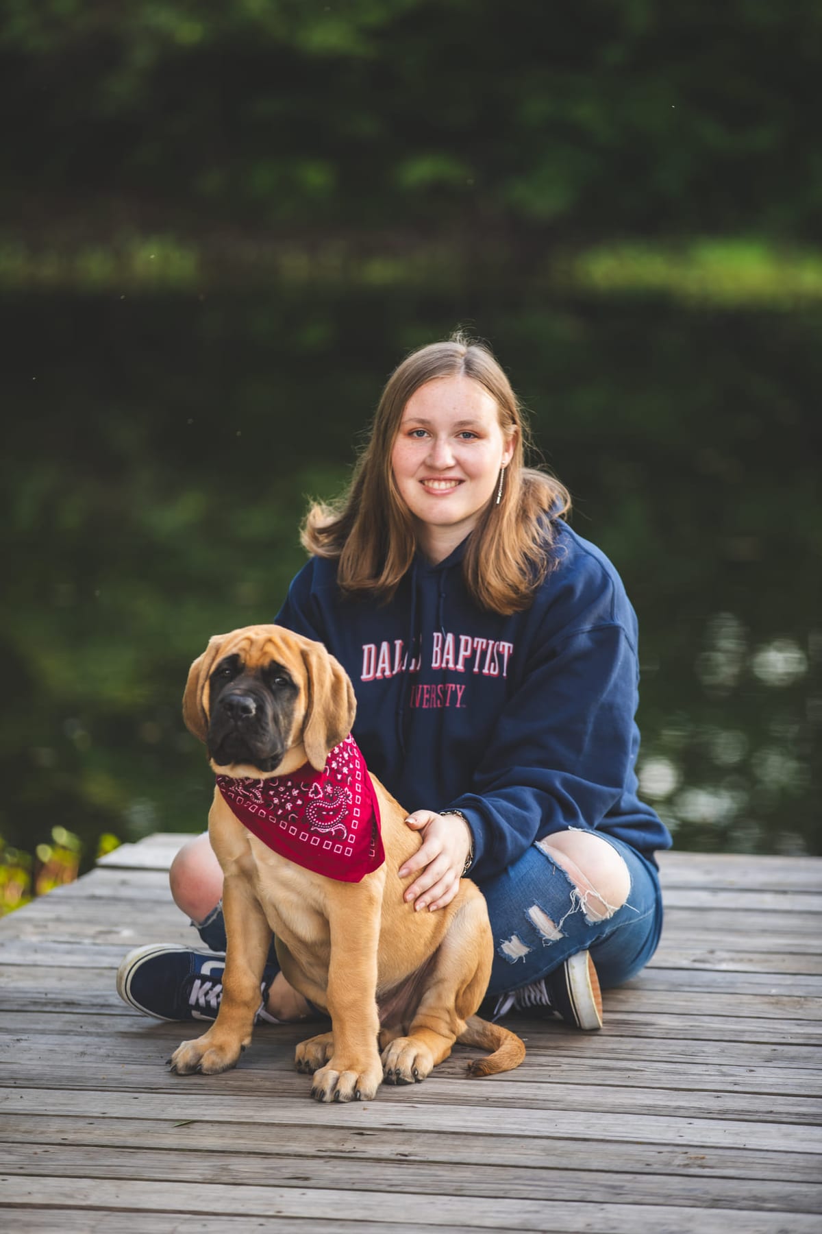 A senior kneeling on a dock beside a mastiff in a bandana.